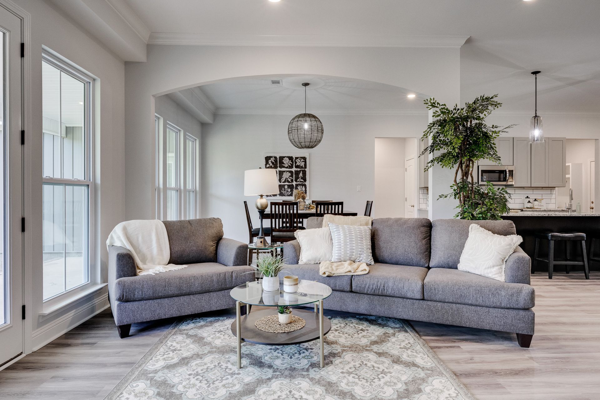 Living room with gray furniture, white walls, and arched doorway, showcasing an open floor plan.