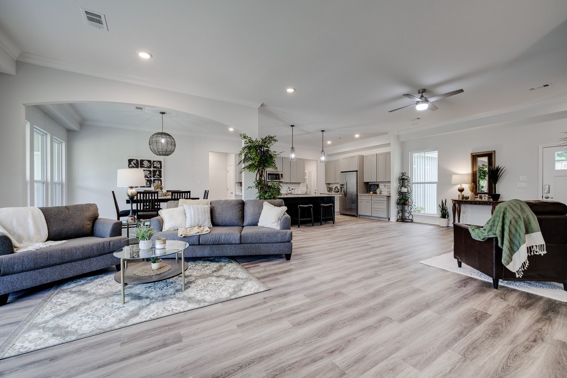 Spacious open-concept living area with gray sofas, light wood floors, and a view of the kitchen and dining area.