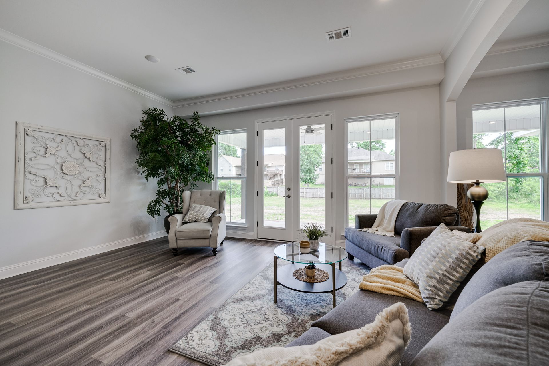 Spacious living room with gray couch, armchair, and French doors. Neutral color scheme, wood floors, and abstract art.