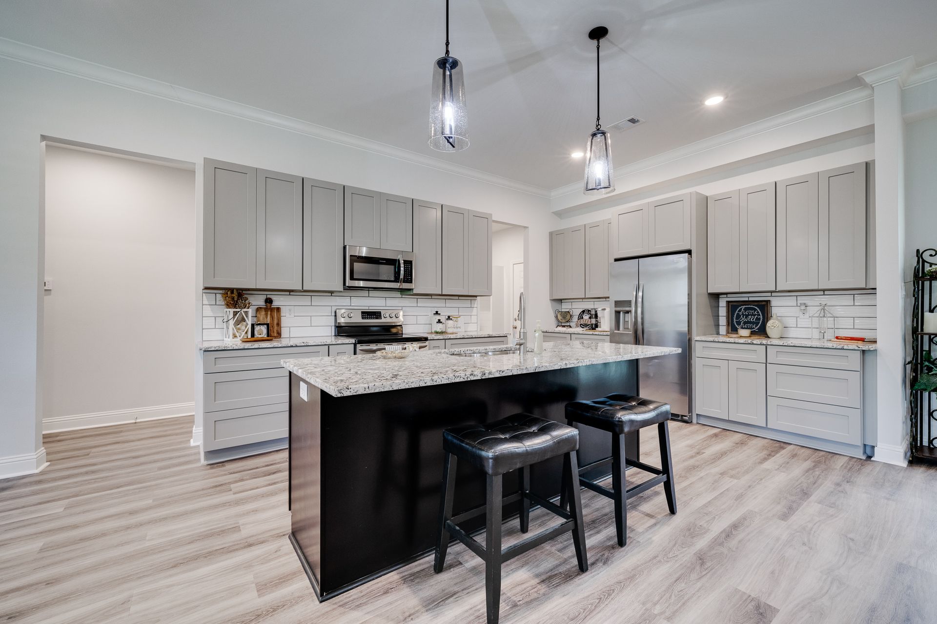Modern kitchen with gray cabinets, black island, stainless steel appliances, and light wood flooring.
