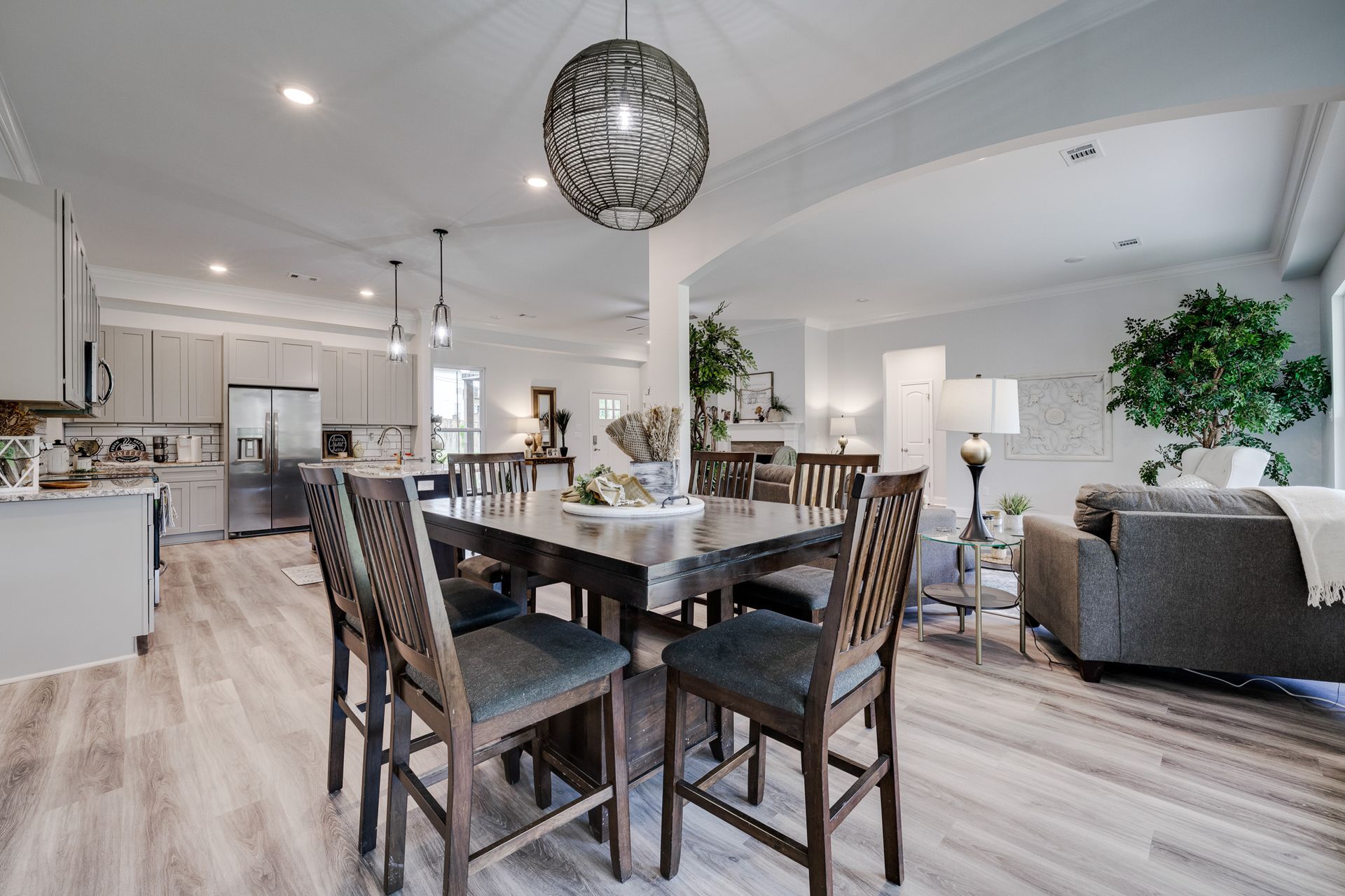 Open-concept dining room with a dark square table, gray chairs, and modern light fixture.