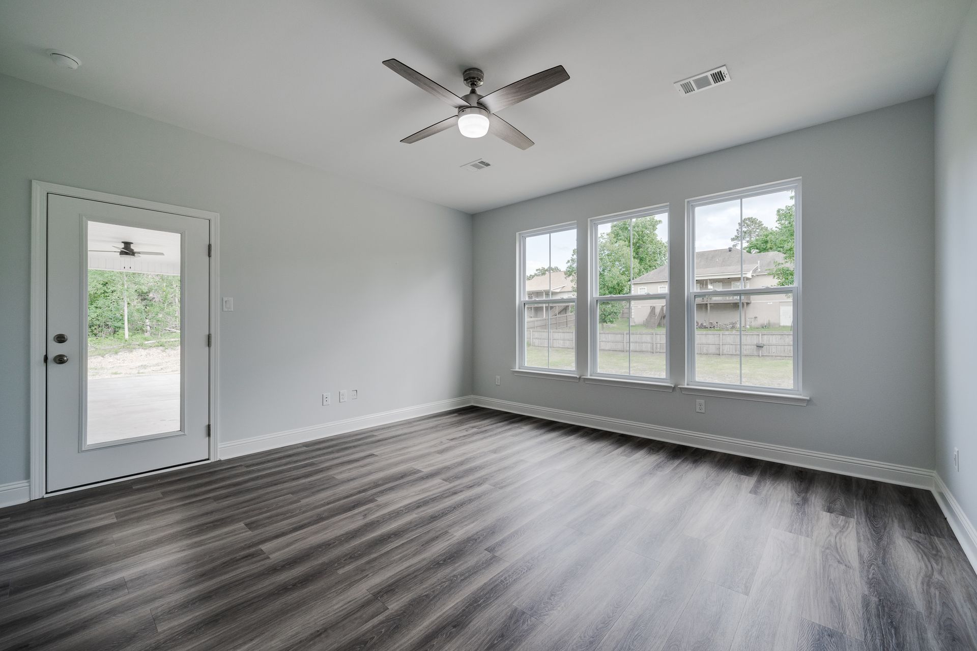 Empty room with gray walls, wood-look floor, windows, and a ceiling fan.