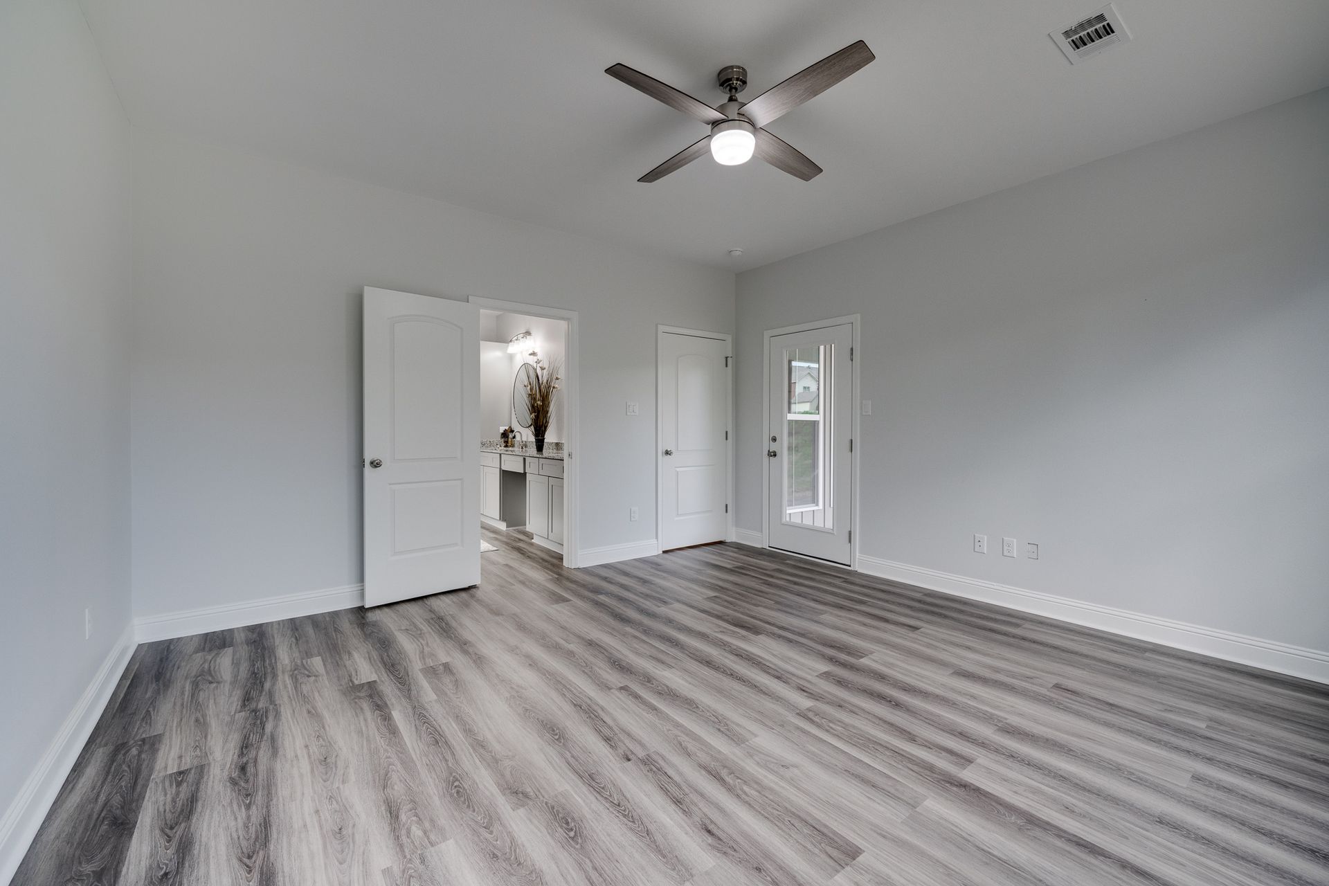 Empty bedroom with gray wood-look flooring, light gray walls, white trim and doors, and a ceiling fan.