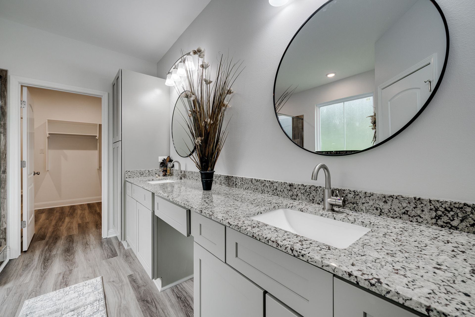 Bathroom with double vanity, granite countertop, large round mirror, and walk-in closet.