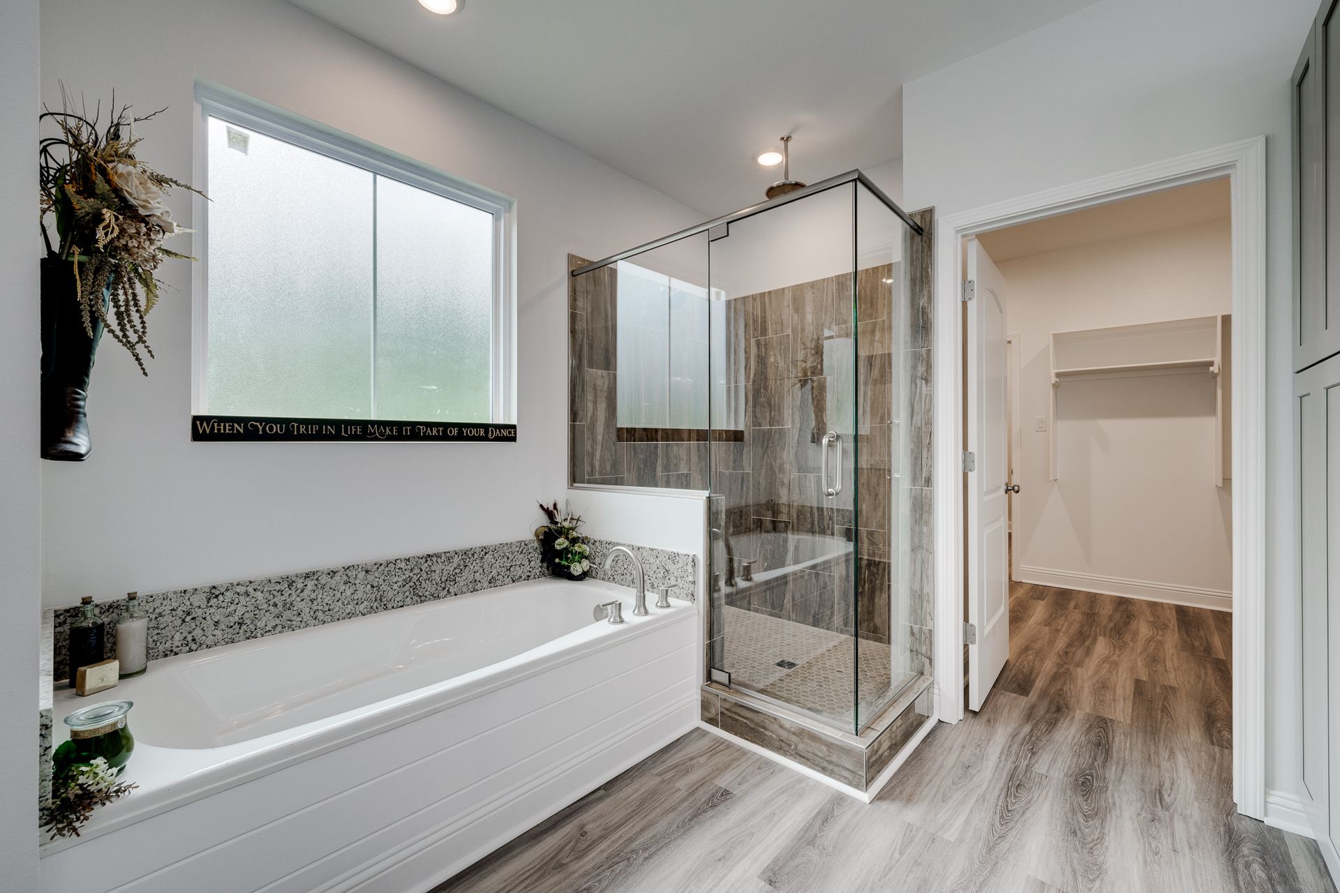 Modern bathroom with bathtub, shower, and walk-in closet, featuring wood-look floors and neutral colors.