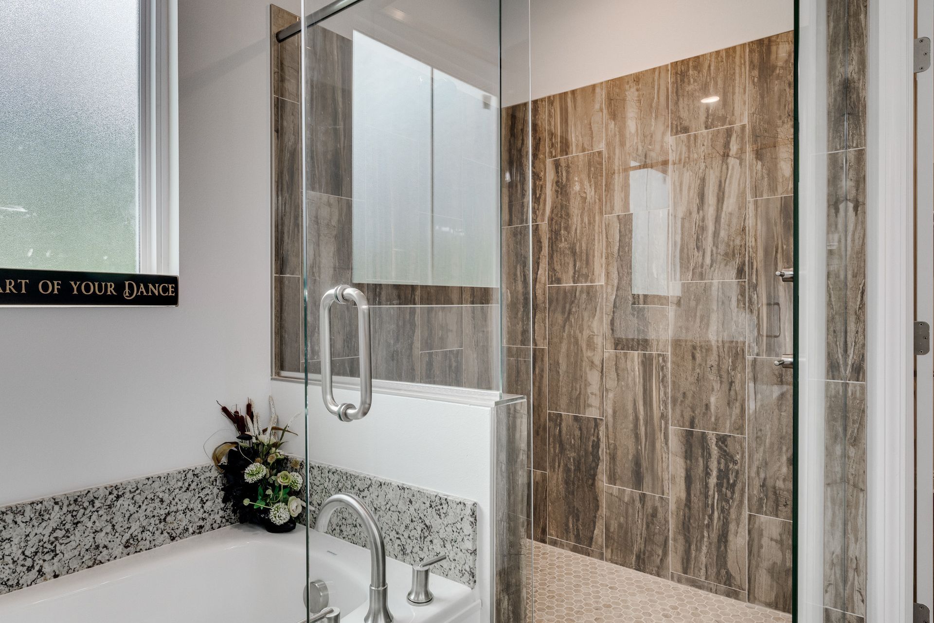 Modern bathroom with a glass shower, gray and brown tiled walls, and a bathtub with mosaic tile.