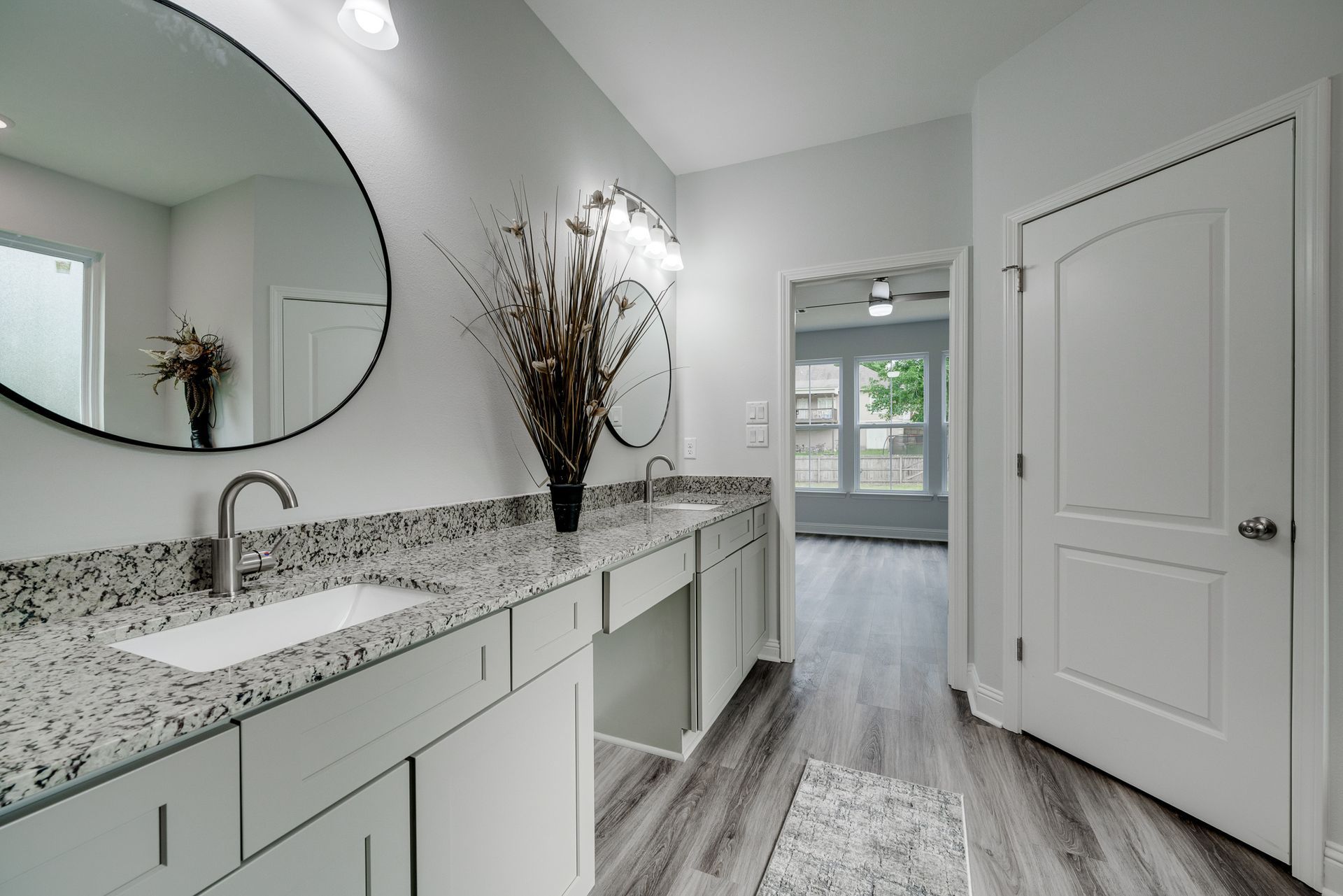 Bathroom with white cabinets, granite countertop, large round mirrors, and gray flooring.