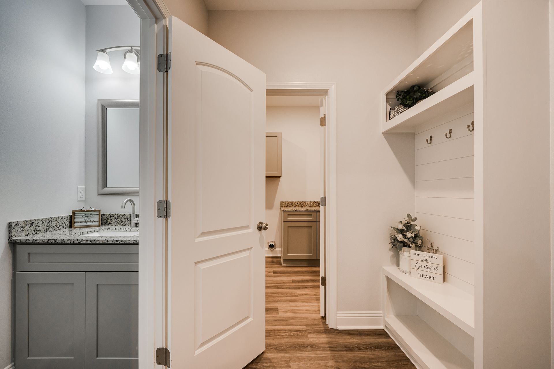 Bathroom doorway with a gray vanity, open white door to a laundry room, and a white built-in storage unit.