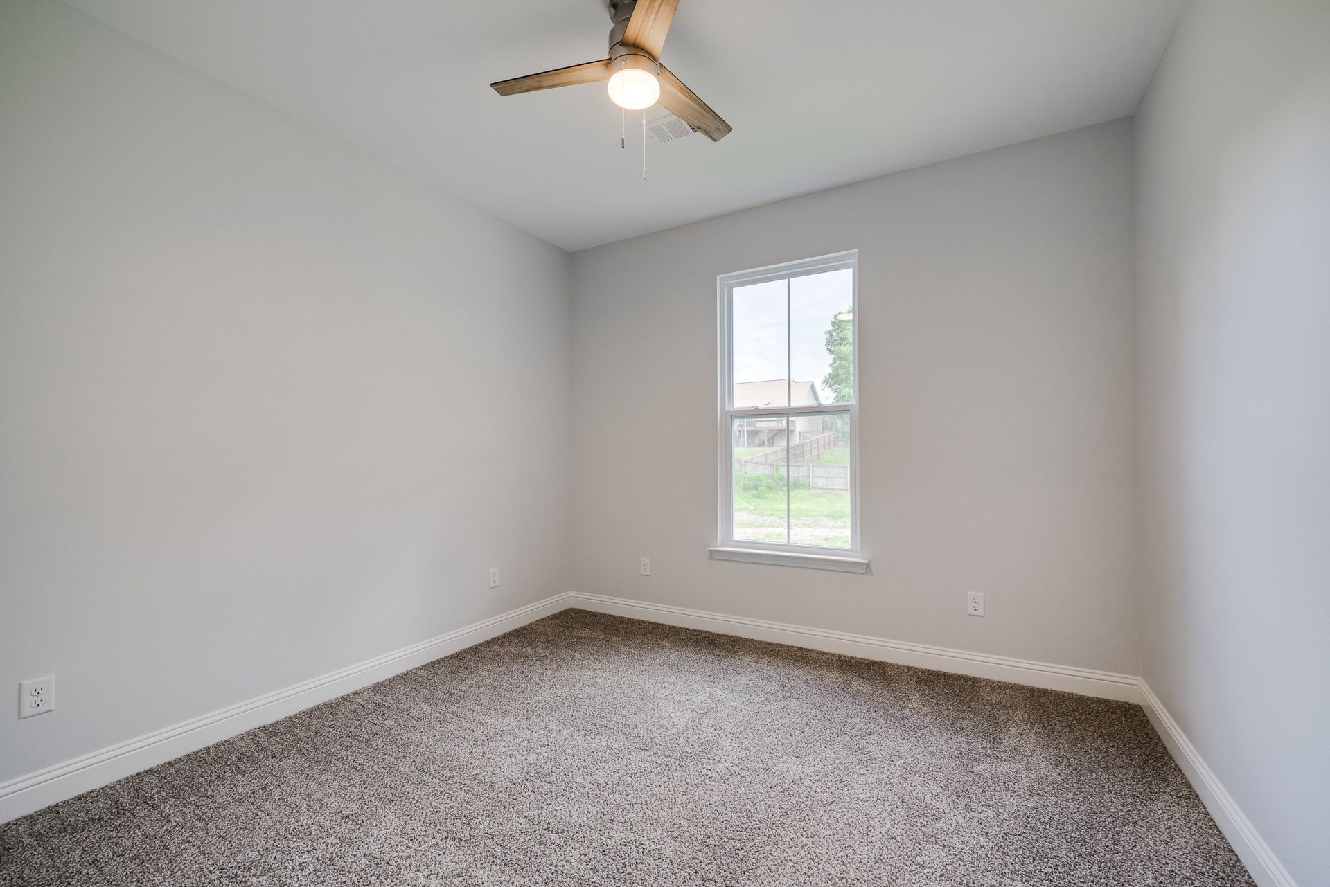 Empty bedroom with gray walls, a window, and a ceiling fan with a brown carpet.