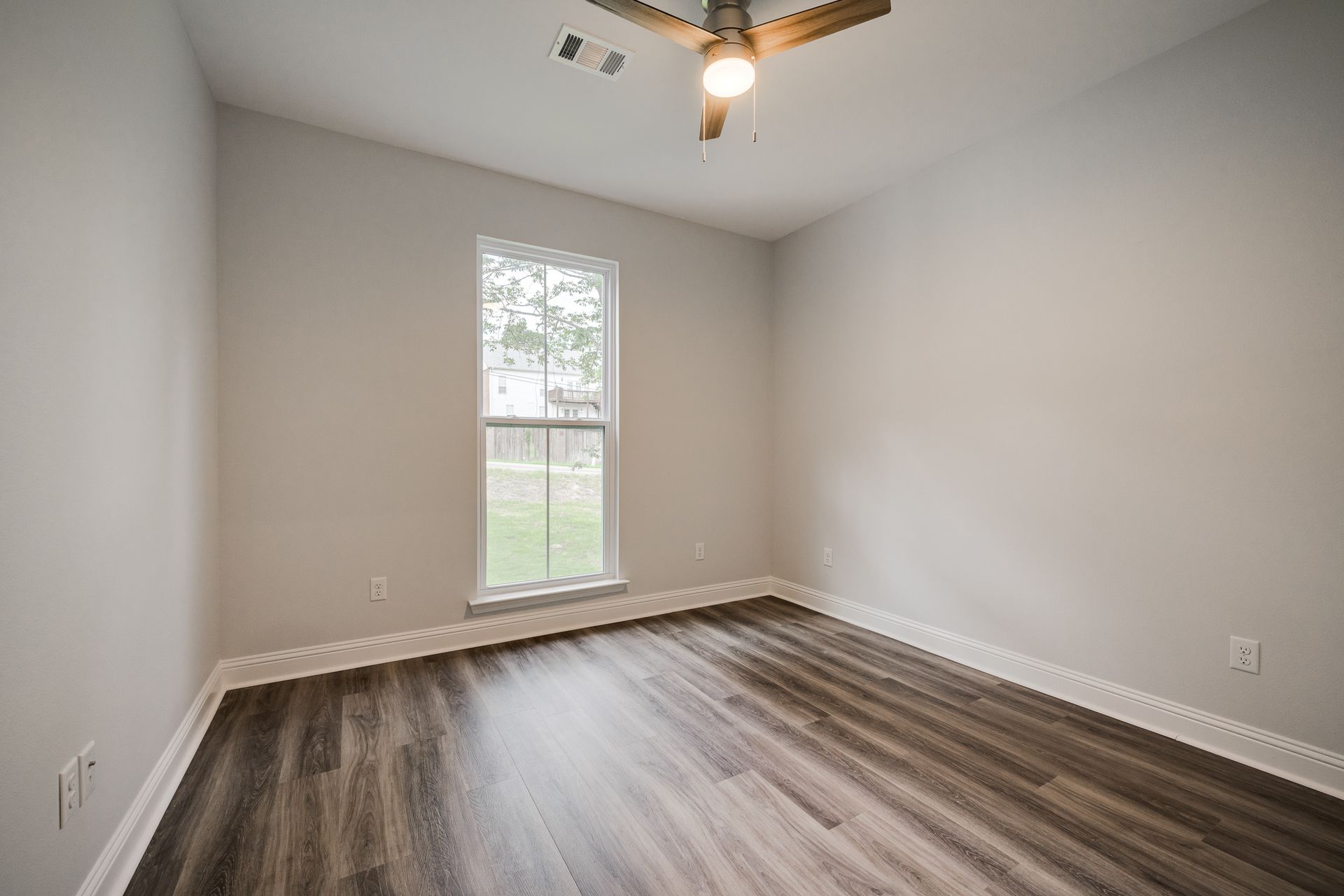 Empty bedroom with gray walls, wood-look floor, and window.