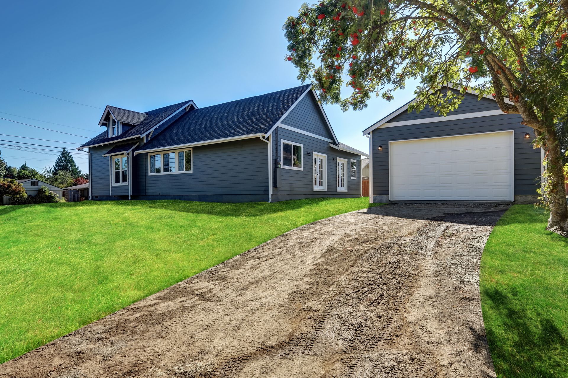 Detached garage beside a residential home with an unfinished driveway