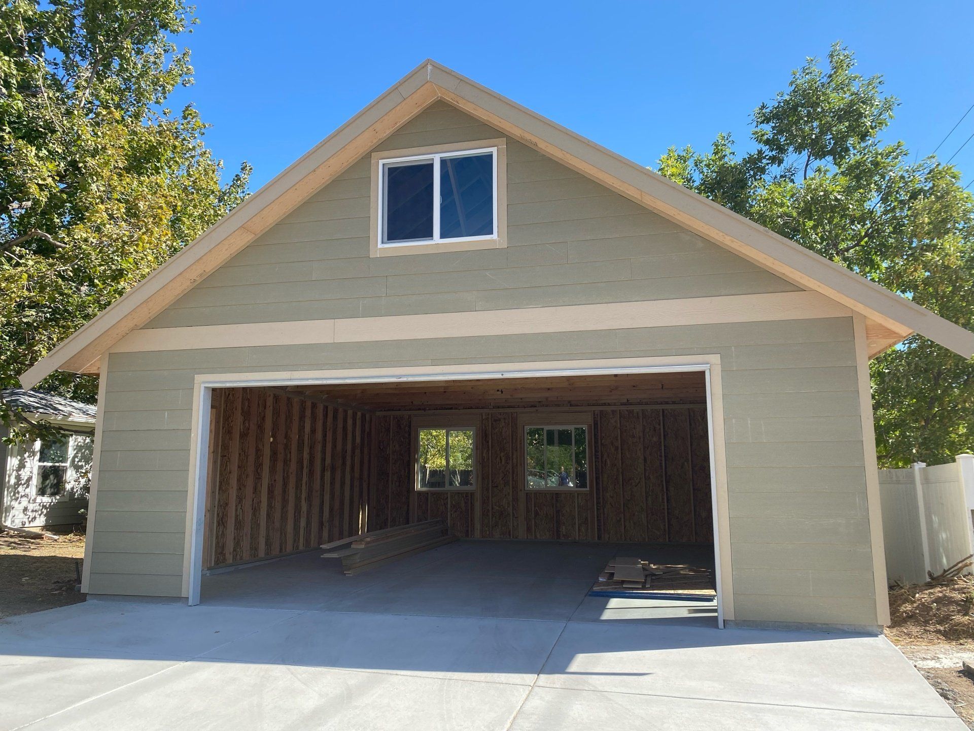 Light green garage with open door, concrete driveway, and small window.