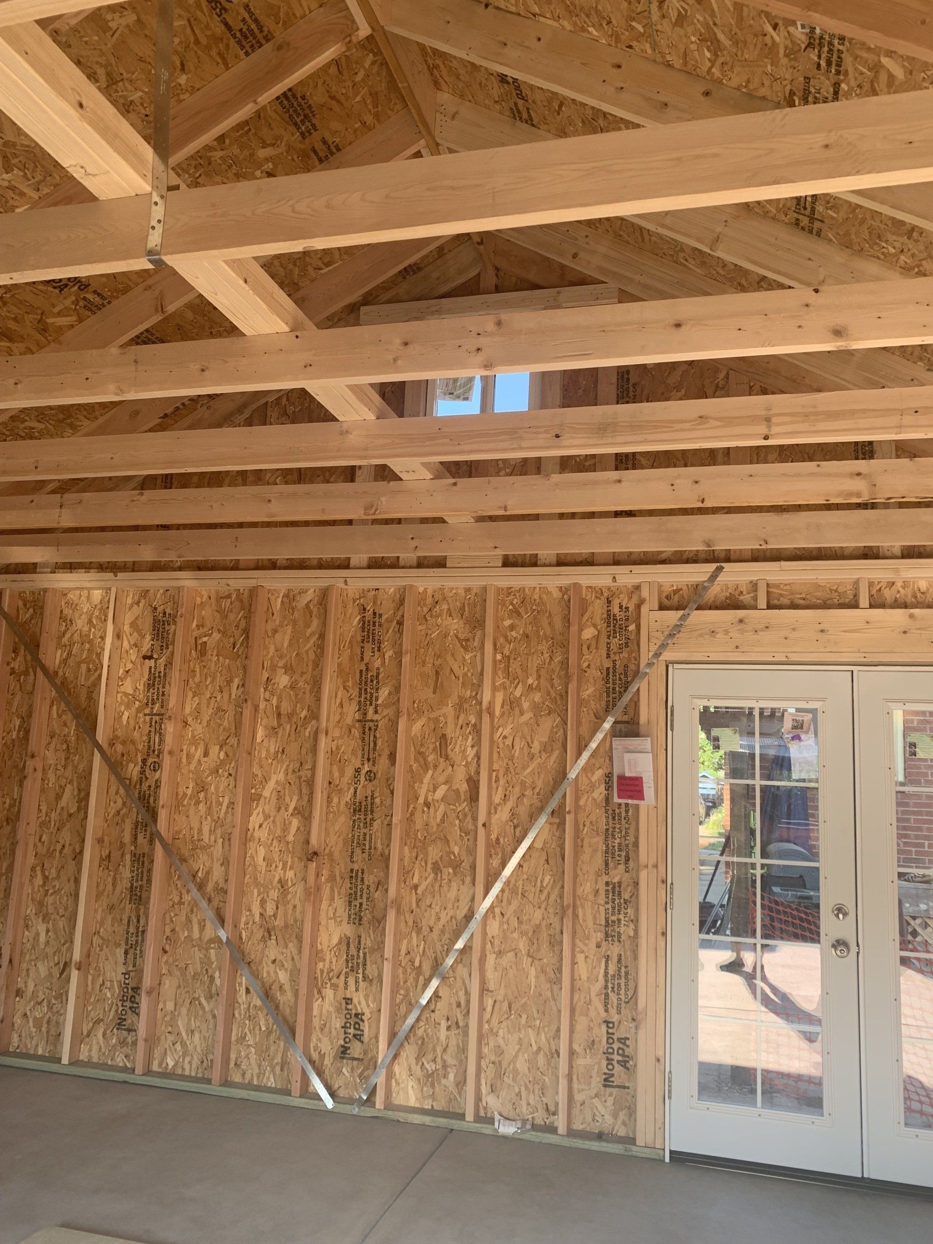 Interior view of a wood-framed structure with exposed beams and an OSB wall, light streaming in.