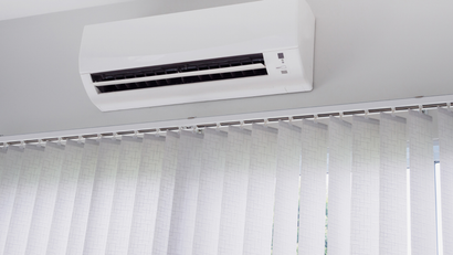 A white wall-mounted air conditioner positioned above vertical white window blinds.