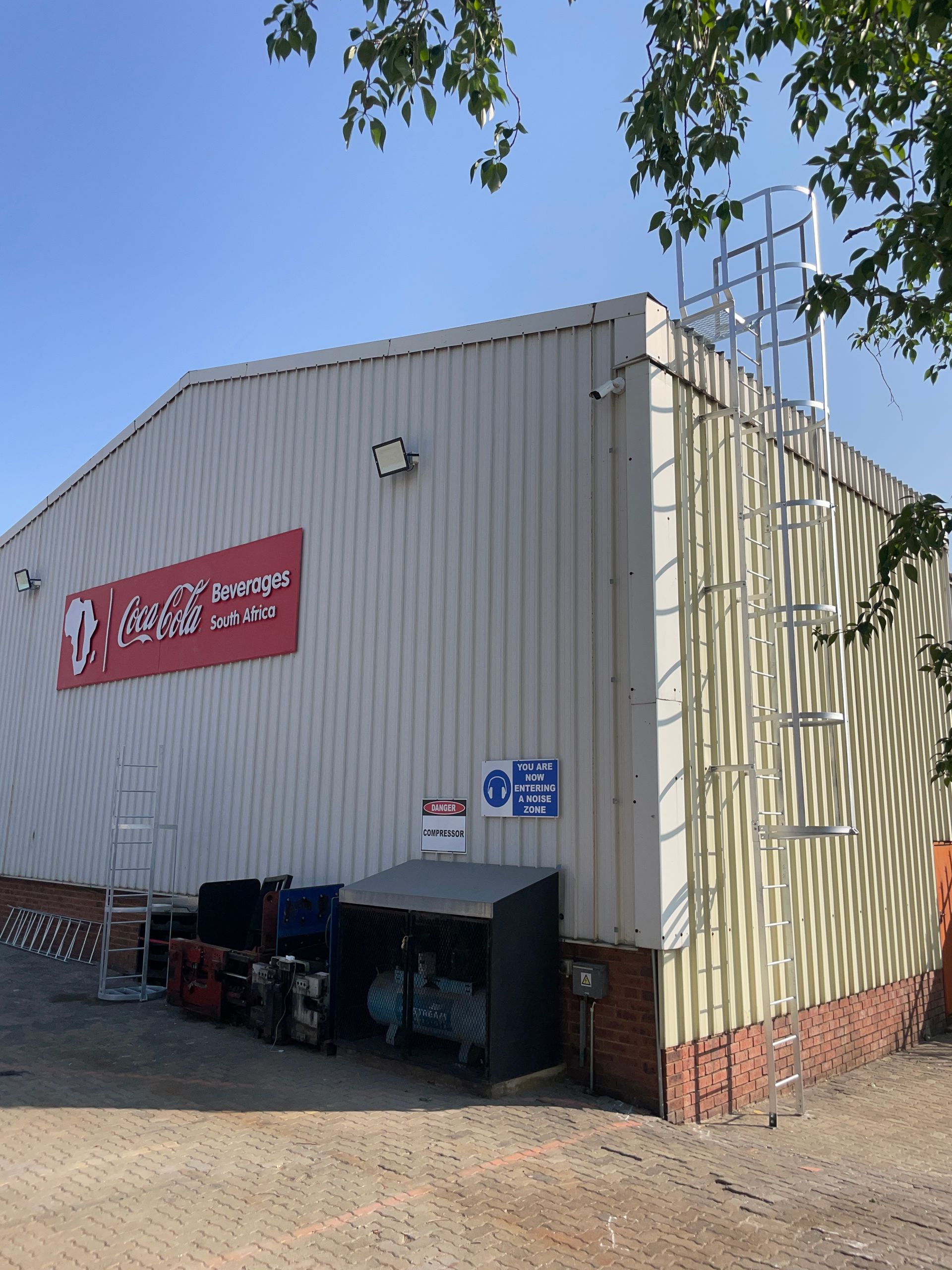 Building with red sign; ladder to roof, gray metal siding, brick base, and clear sky.
