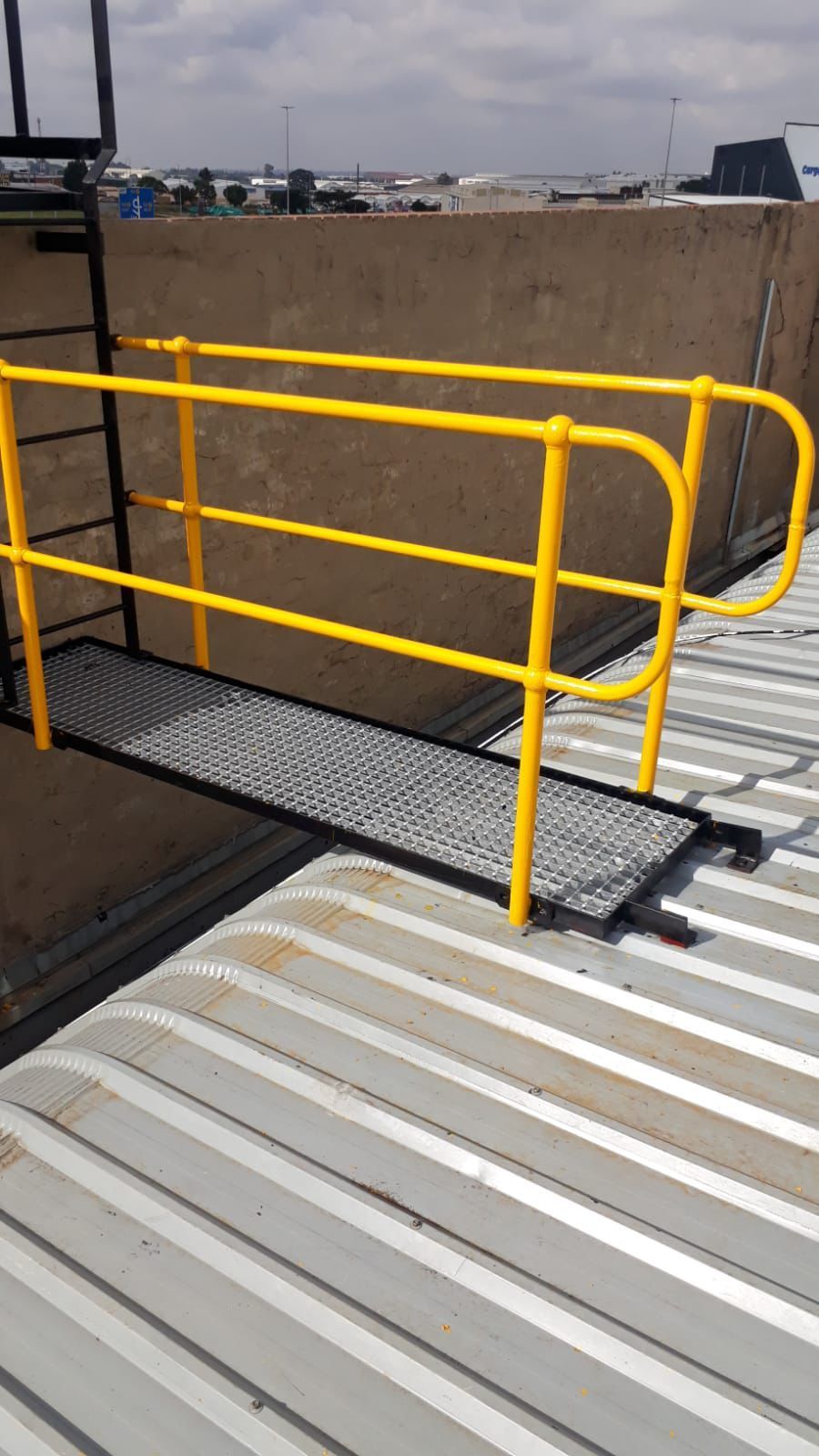 Yellow-railed walkway extends from a metal platform, over a corrugated metal roof.