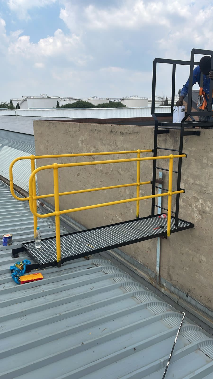 Yellow handrail on rooftop platform with ladder. Person in harness at top.