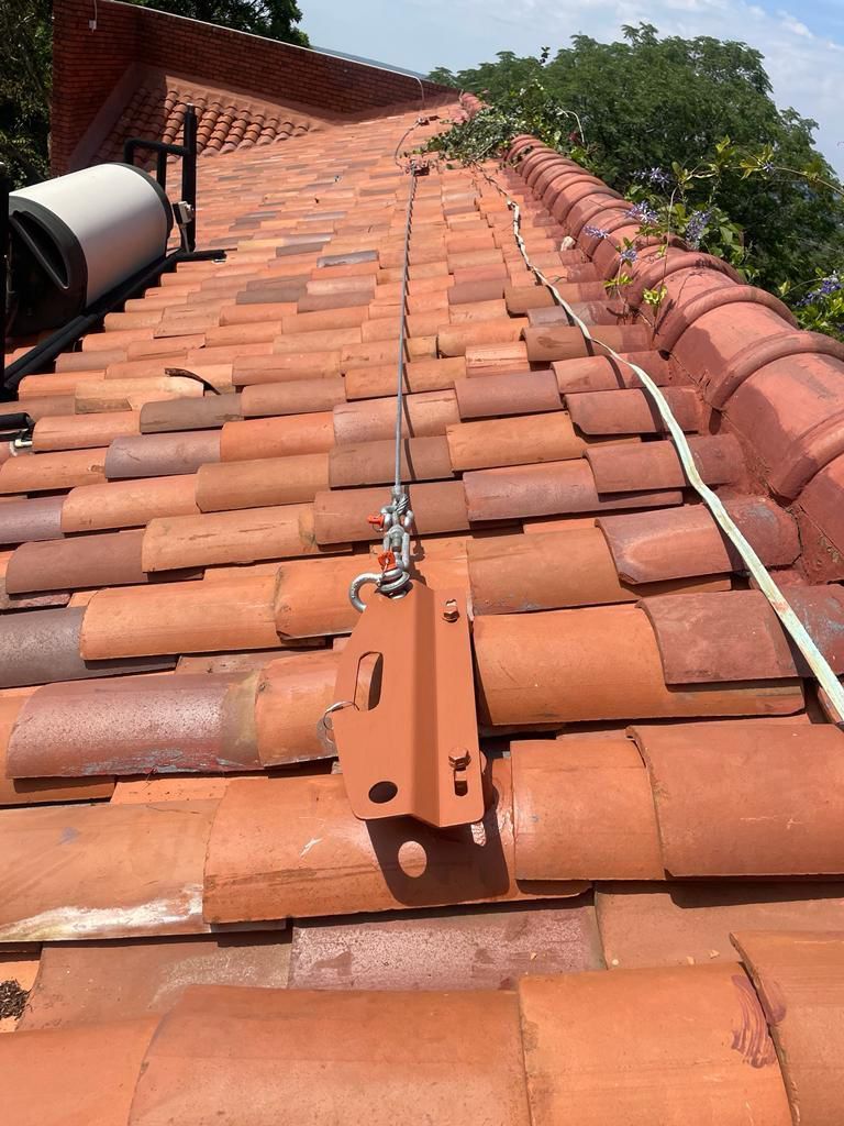 A roof with terracotta tiles; a safety cable system is installed. A steel cable runs along the roof’s ridge.