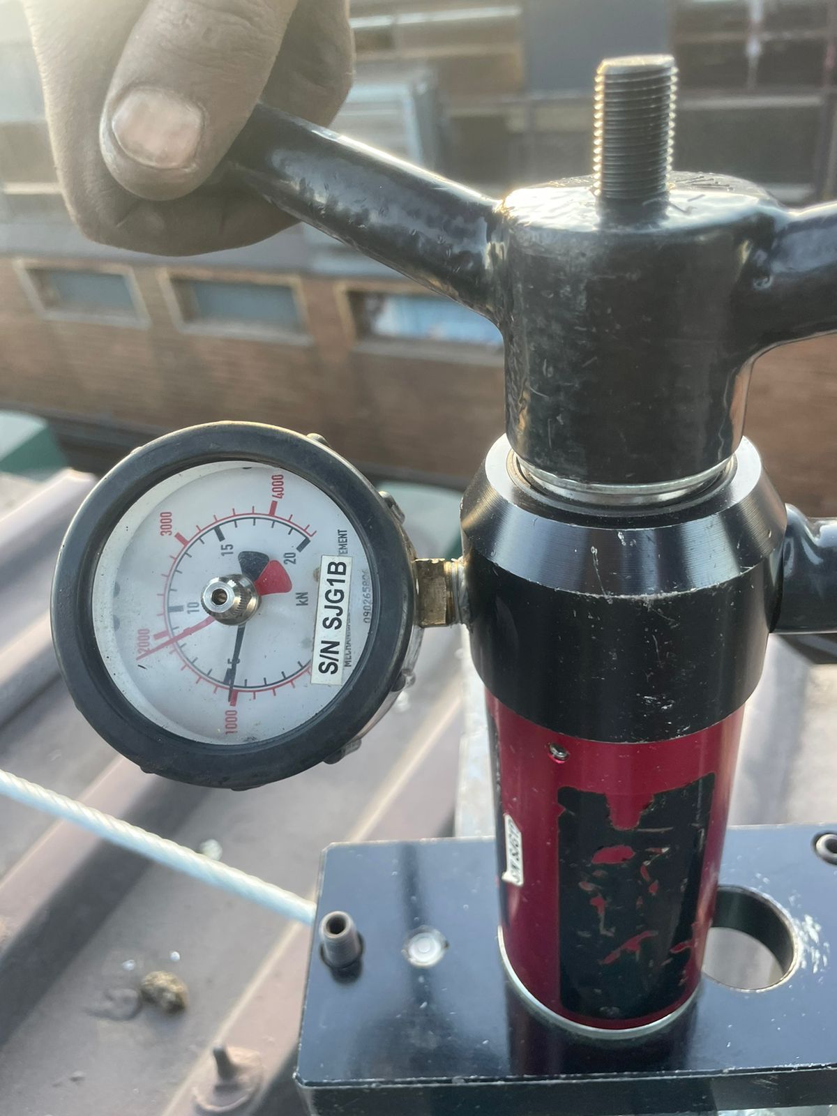 A person's hand turning a valve on a black and red pressure regulator with a gauge showing pressure.