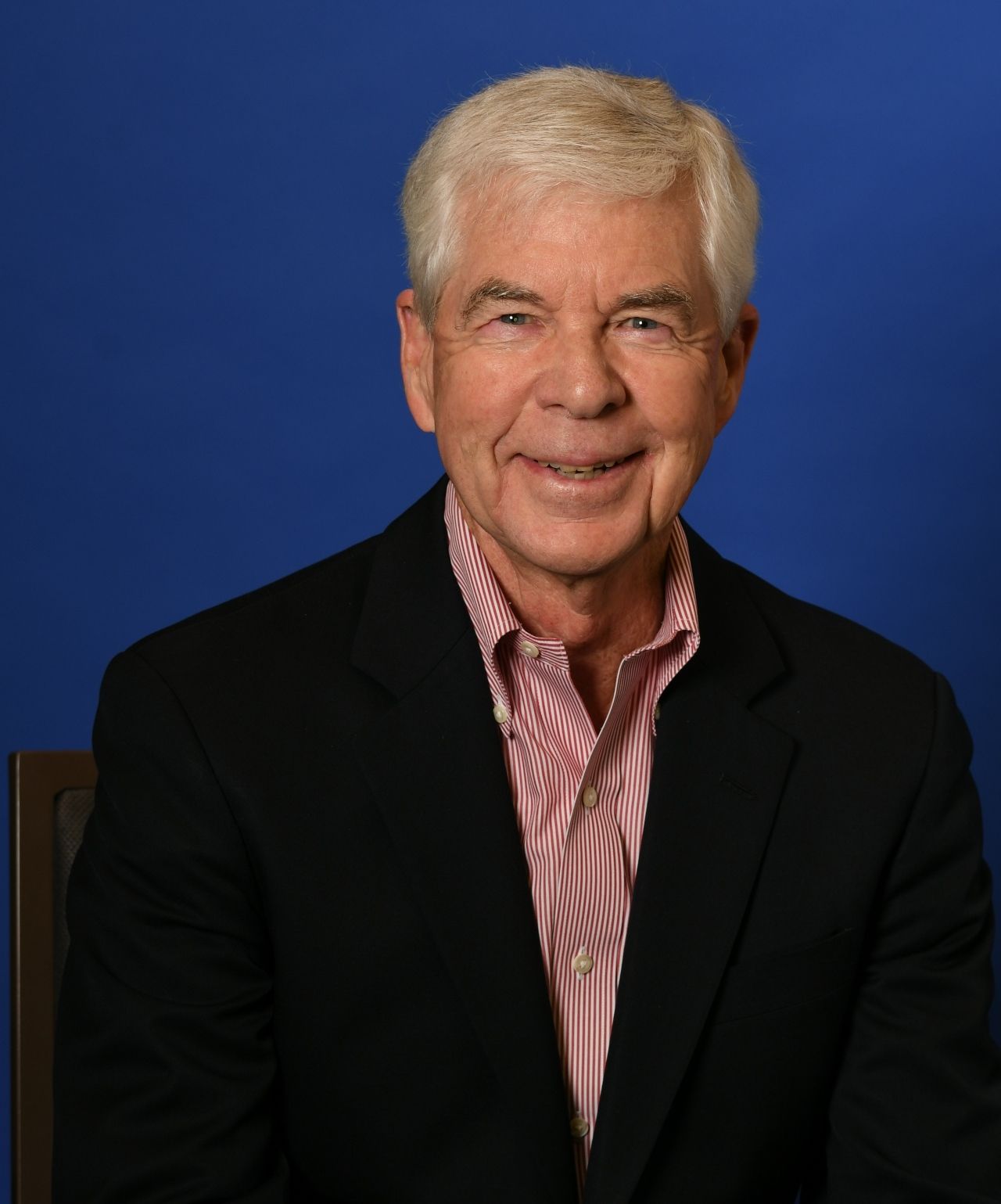 Chip Rohde is wearing a black blazer and striped shirt, posed against a blue studio background.