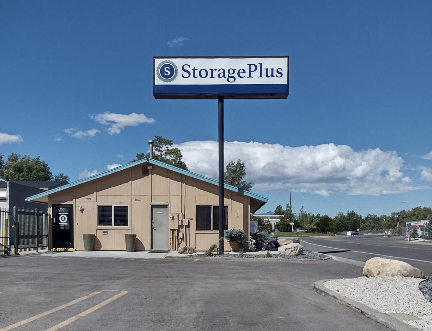 StoragePlus sign above a small tan building with parking in front, under a blue sky.