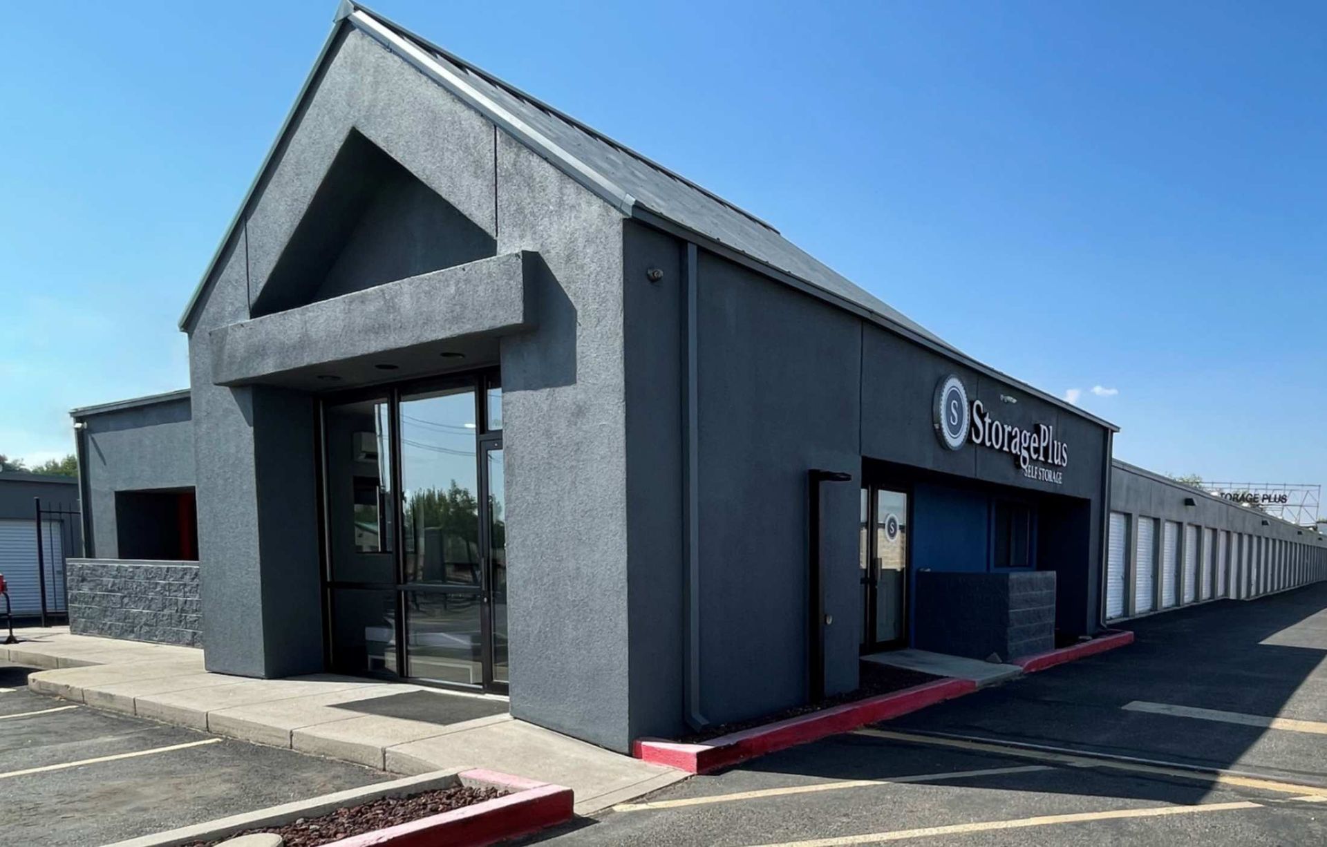 Exterior of a storage facility office with a dark gray facade, glass doors, and rows of storage units.
