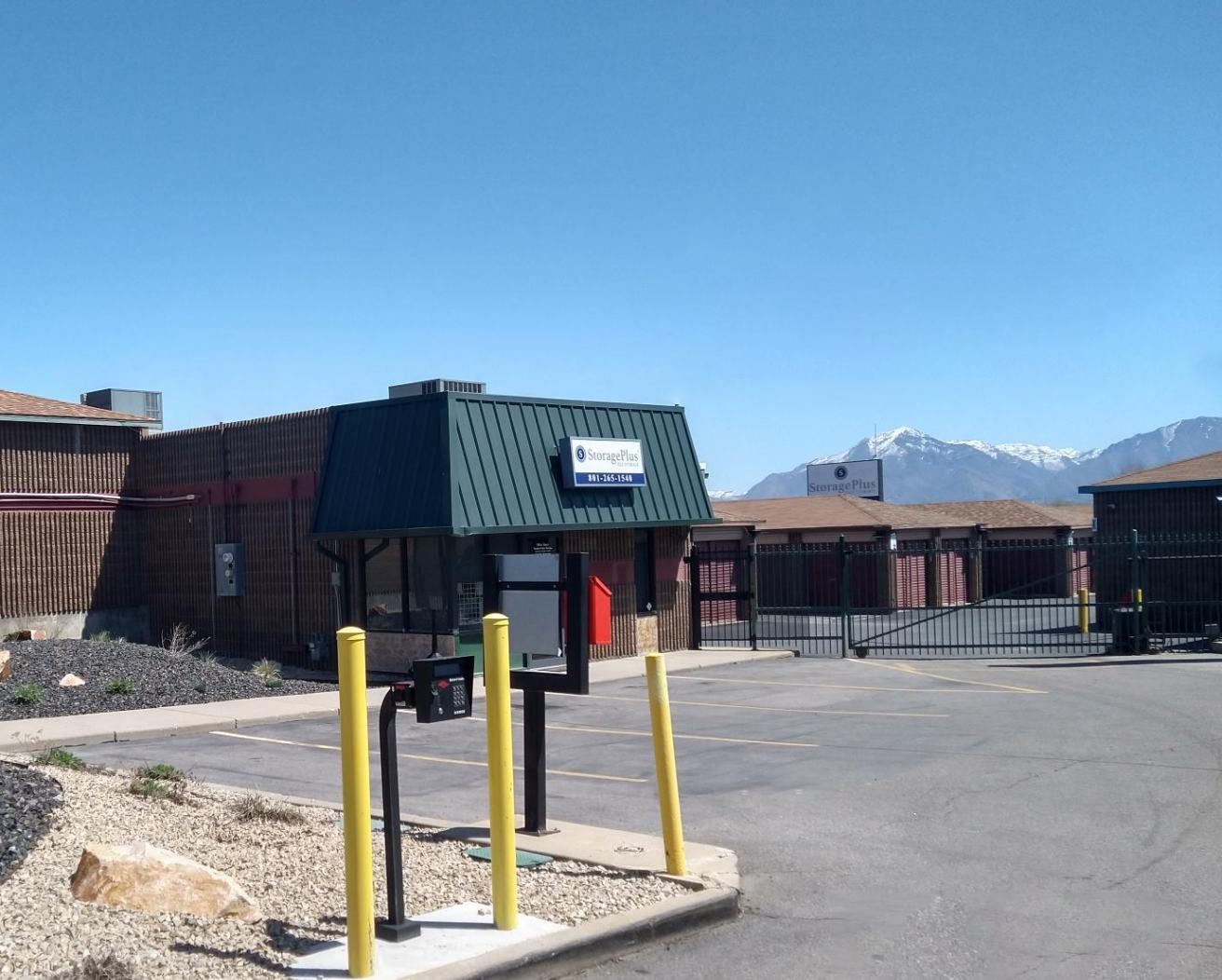 Drive-through storage facility with office, gate, and distant snow-capped mountains. Sunny day.