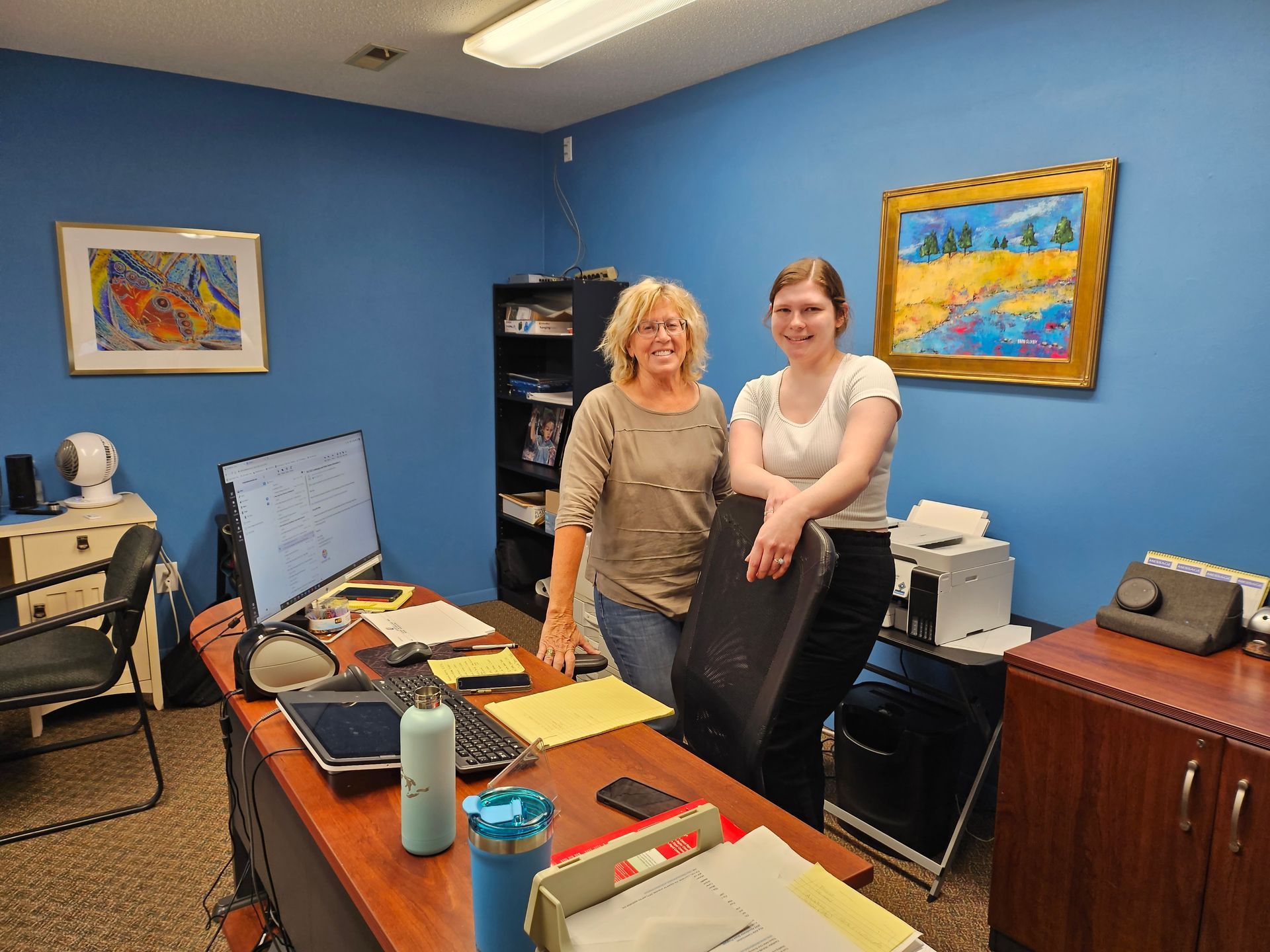 Two women are standing in front of a desk in an office.