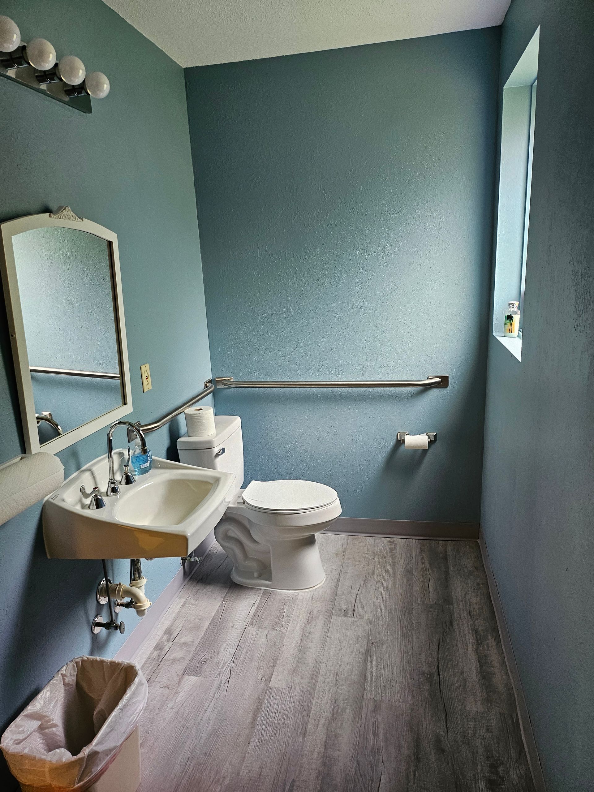 A bathroom with a sink , toilet , mirror and trash can.