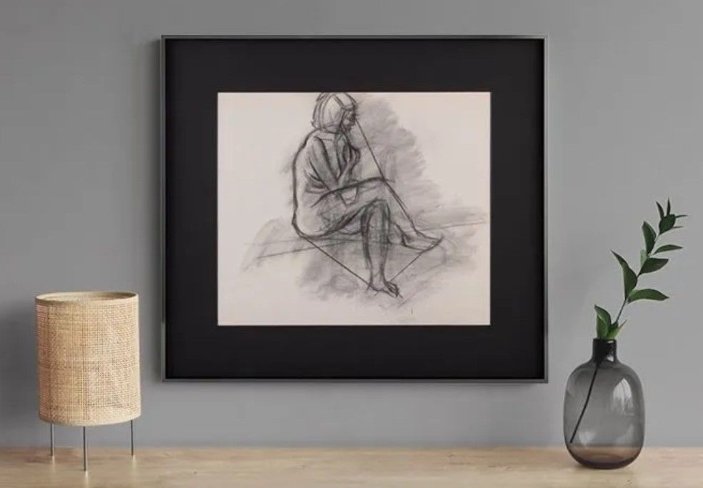 A framed drawing of a woman sitting on a table next to a vase.