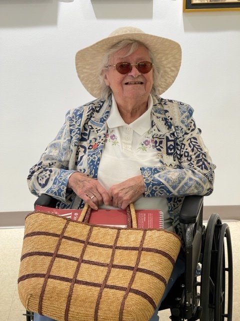 An elderly woman in a wheelchair wearing a hat and sunglasses
