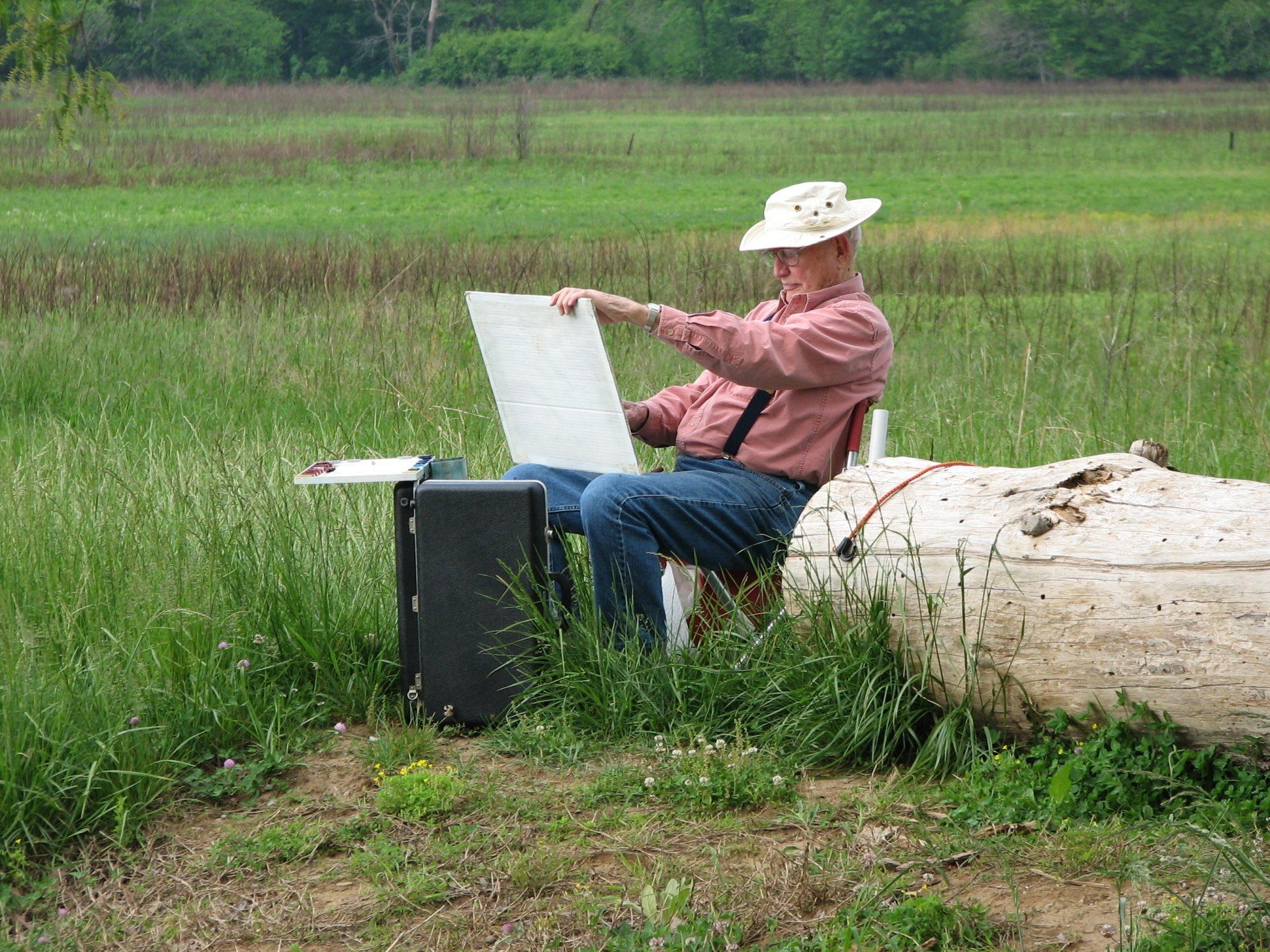 A man is sitting on a log in a field looking at a piece of paper
