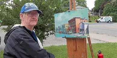 A man is standing in front of an easel with a painting on it.