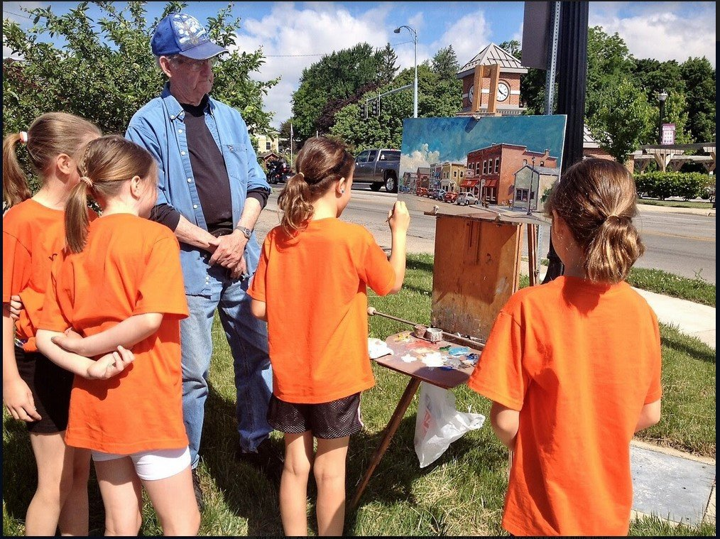 A group of children in orange shirts are looking at a painting