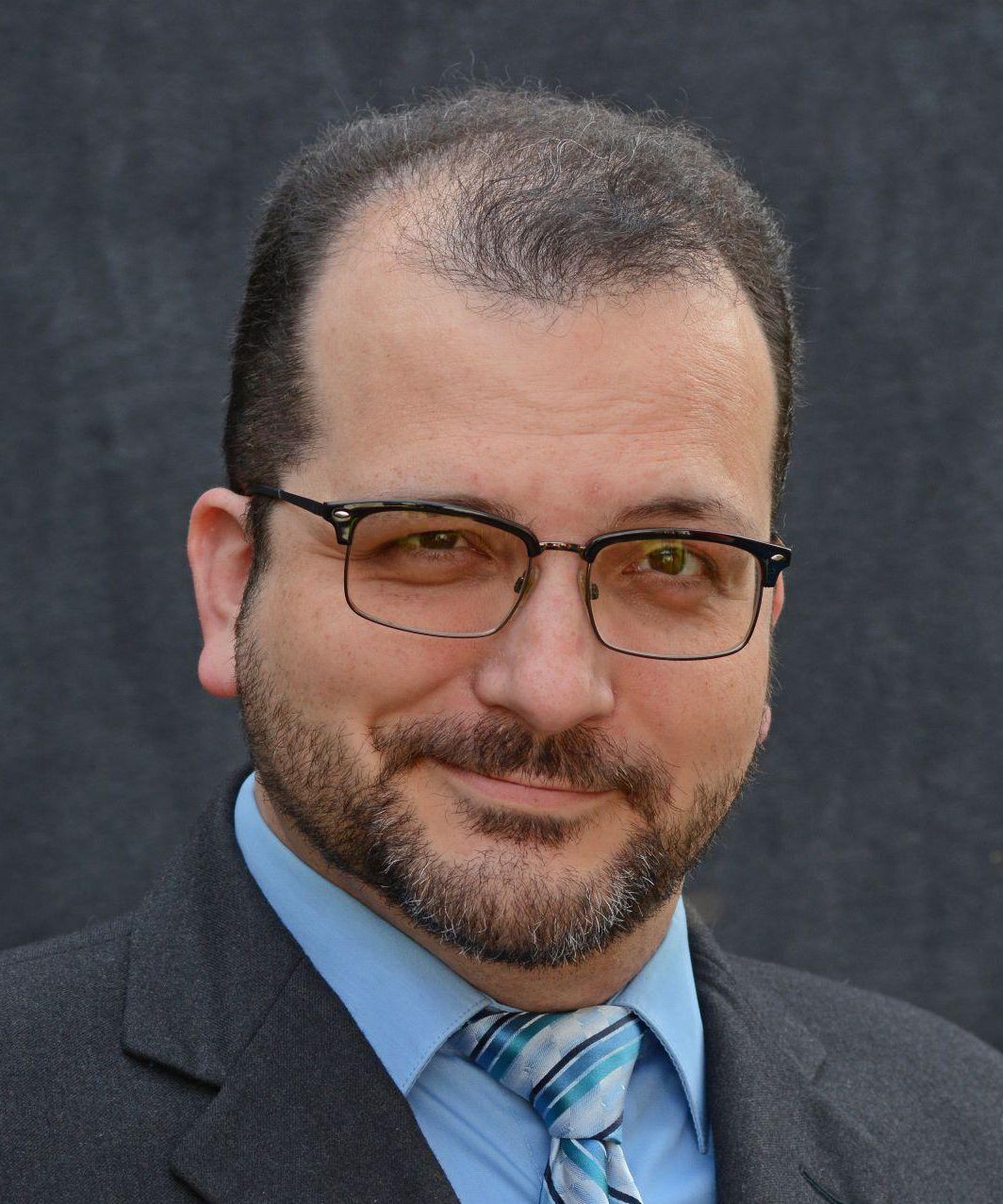 A man with glasses and a beard is wearing a suit and tie
