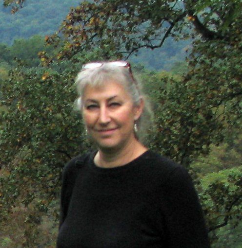 A woman wearing sunglasses and a black shirt is standing in front of trees