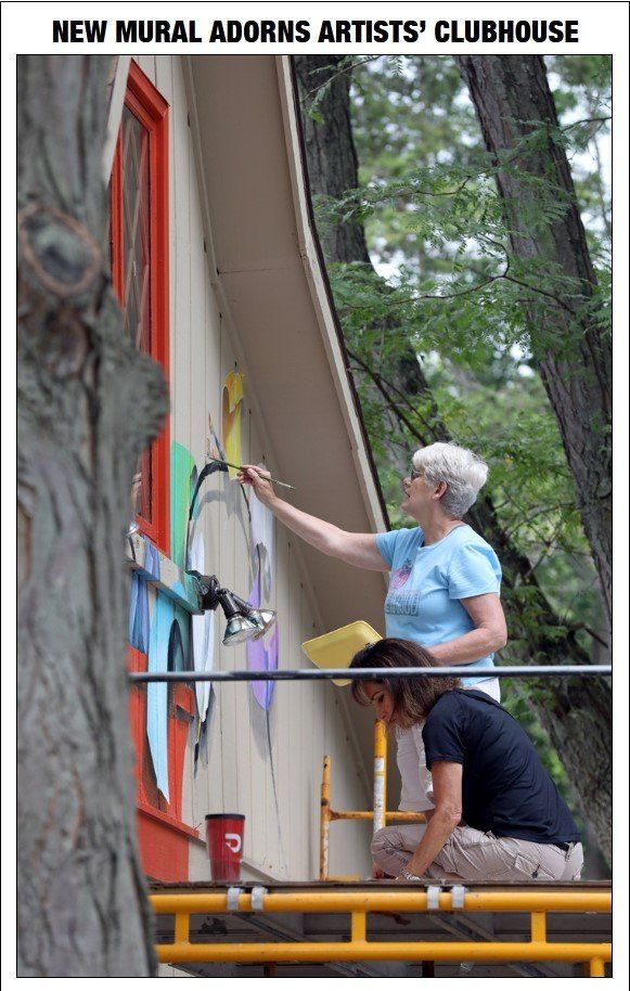 Two women are painting a mural on the side of a building.