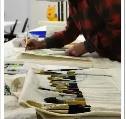 A woman sits at a table painting a picture