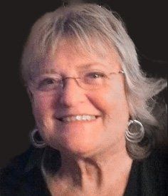 A close up of a woman wearing glasses and earrings smiling.