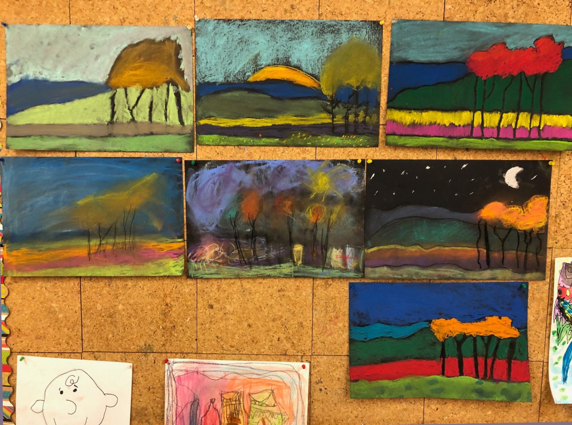 A bunch of paintings are hanging on a cork board