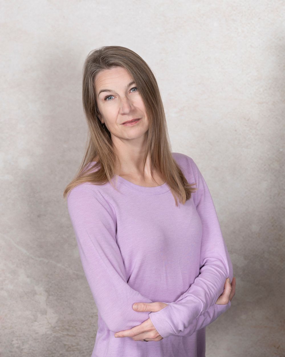 A woman in a purple sweater is standing with her arms crossed.