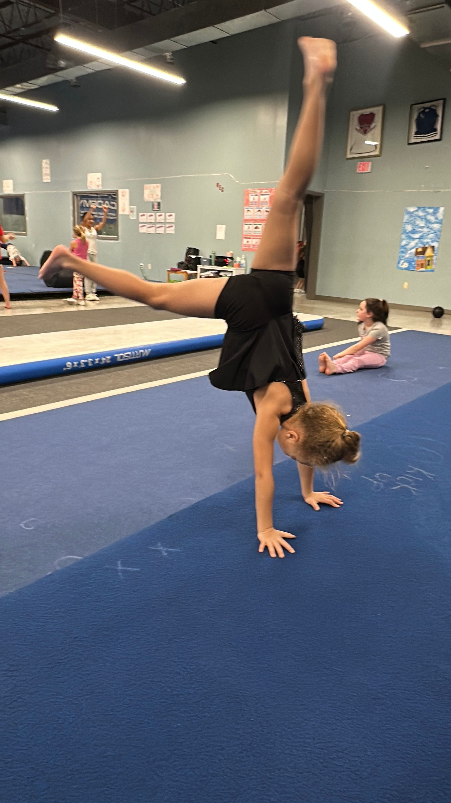 A young girl is doing a handstand on a blue mat in a gym.