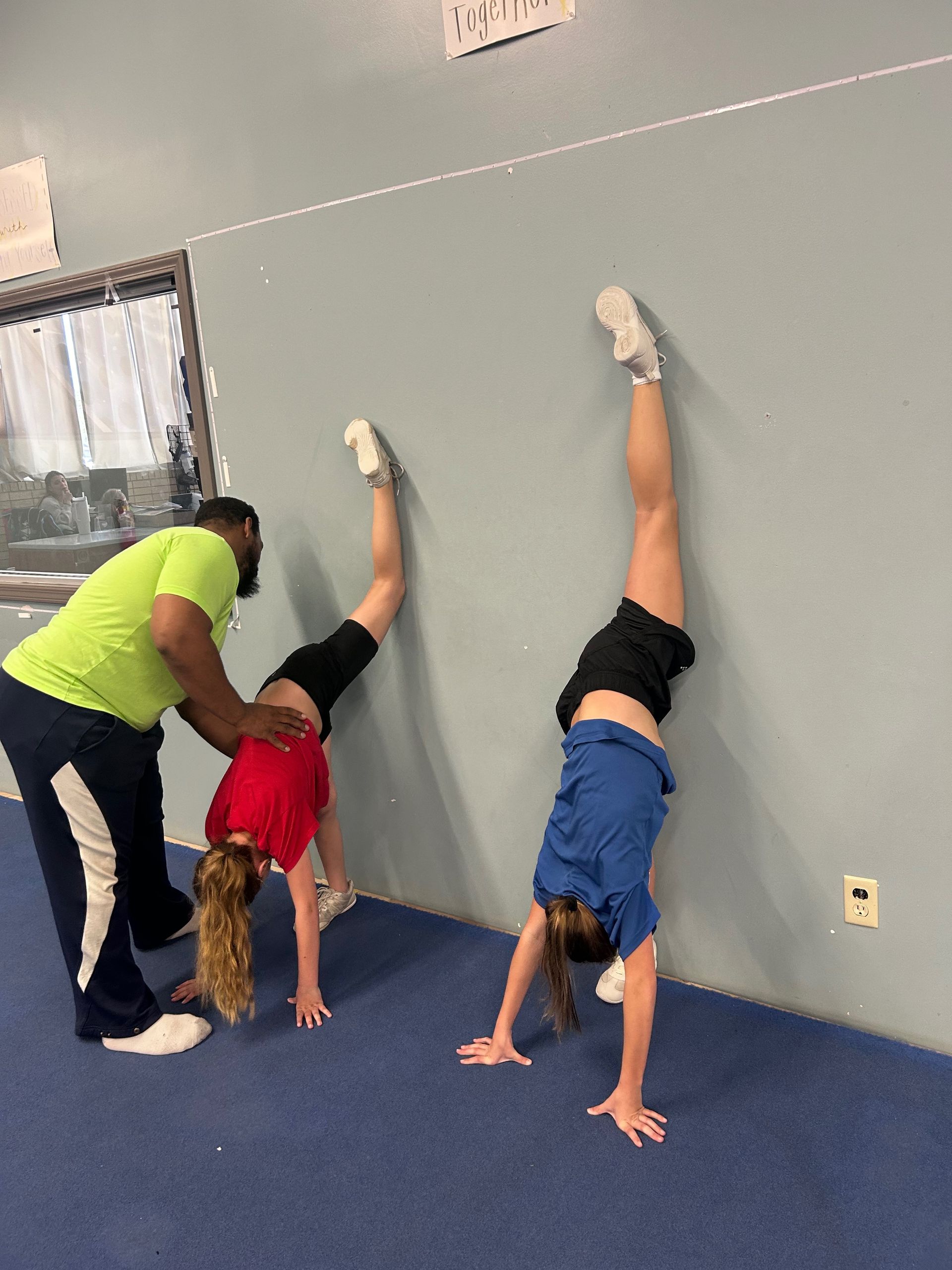 A man is helping a girl do a handstand against a wall.