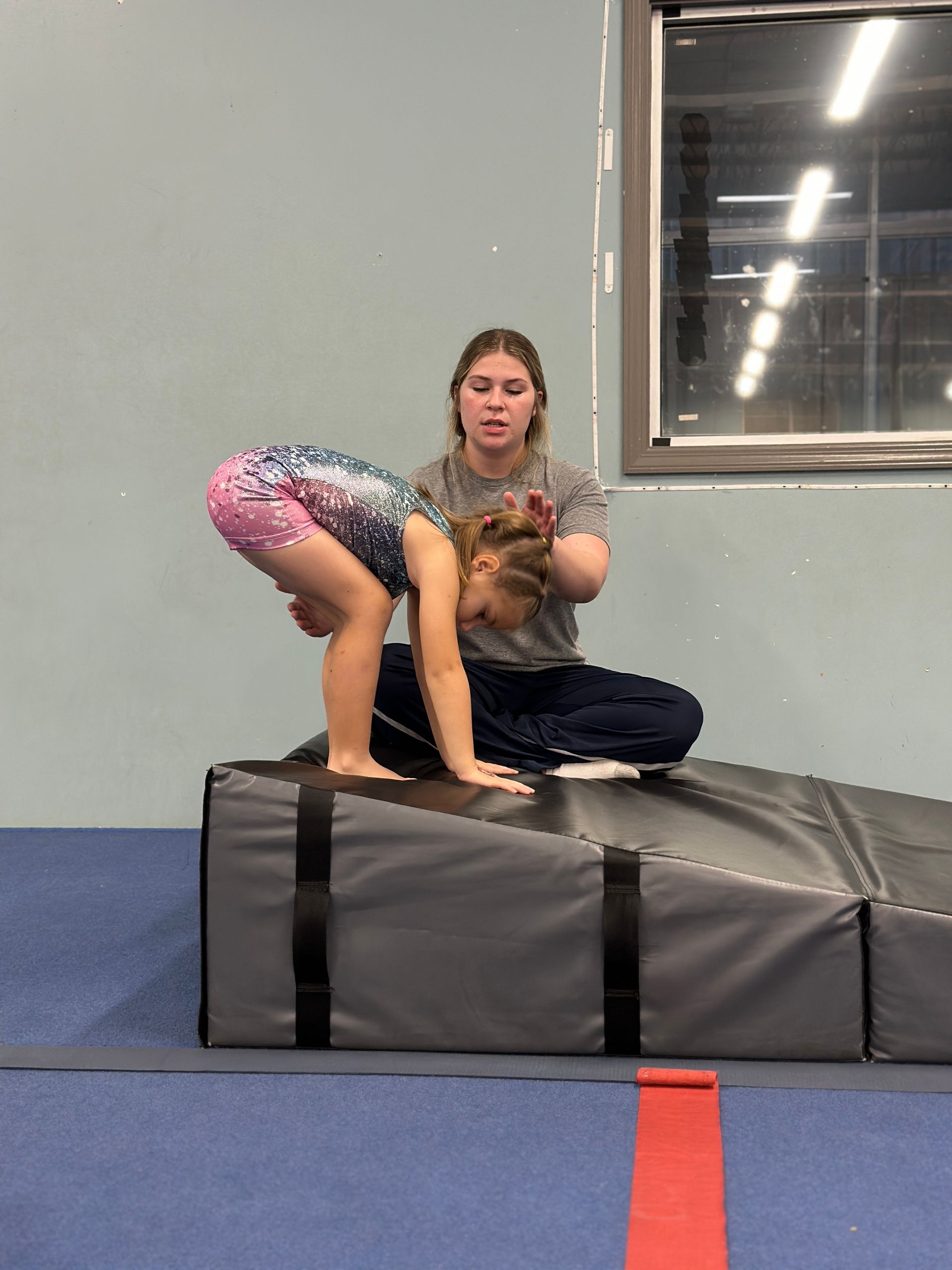 A young girl is doing a handstand on a blue mat in a gym.