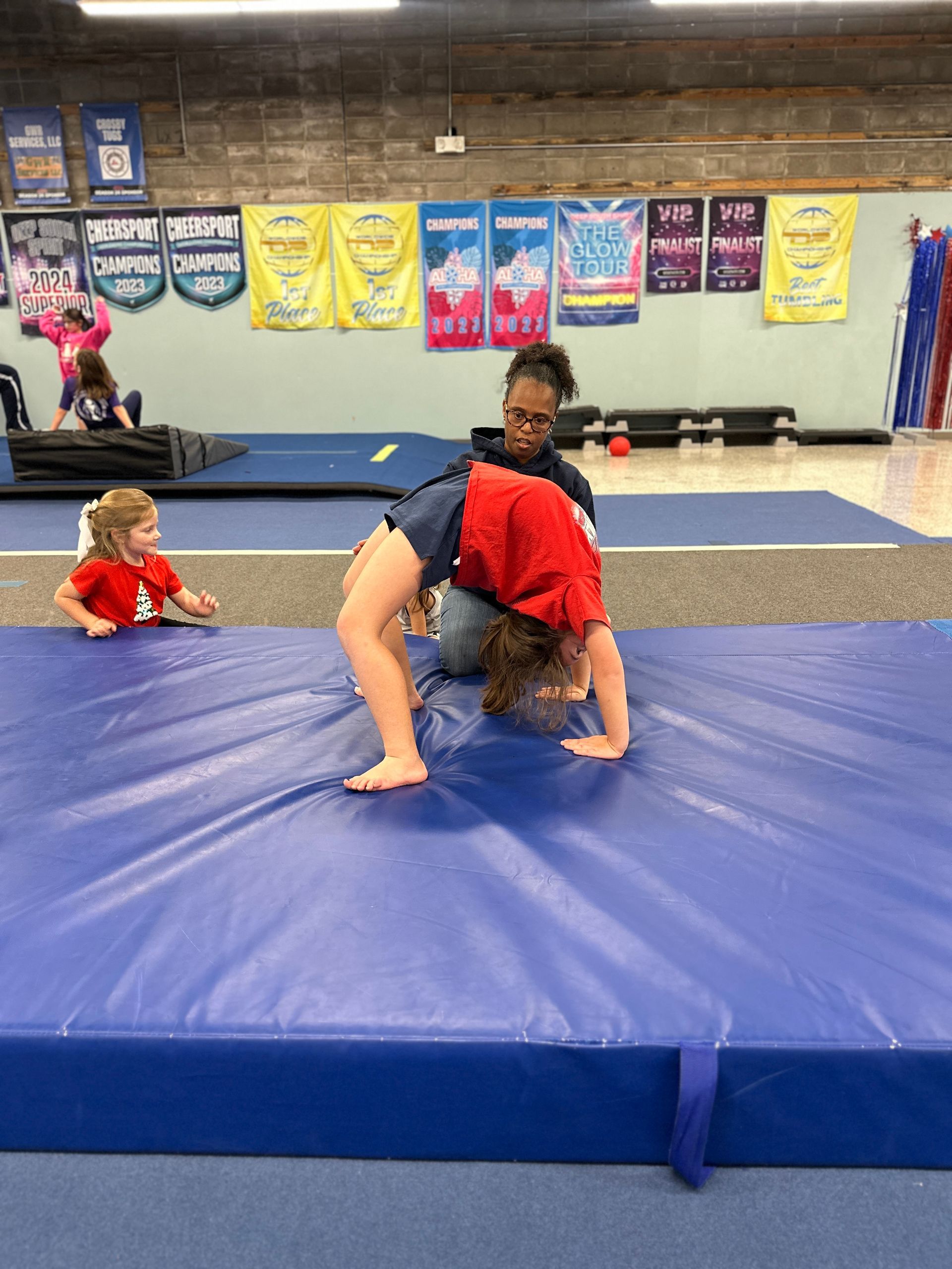 A woman is teaching a child how to do a handstand on a blue mat.