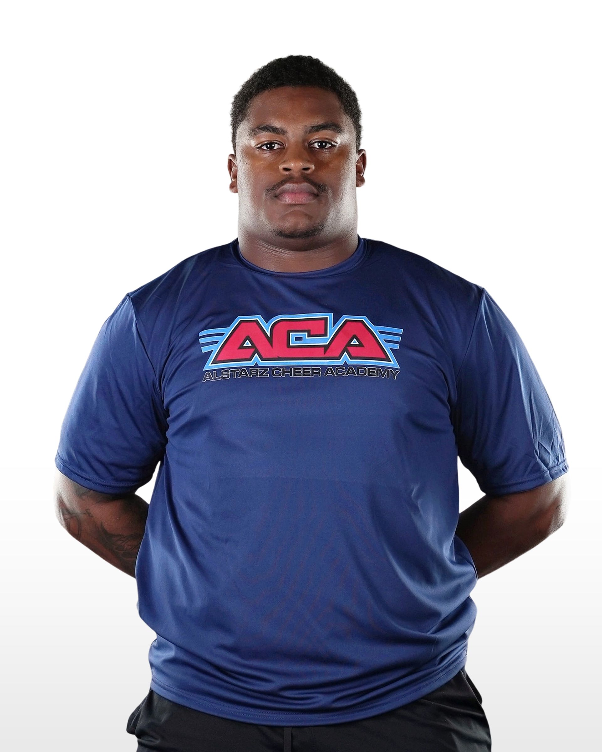 A man wearing a blue aca shirt stands with his hands behind his back