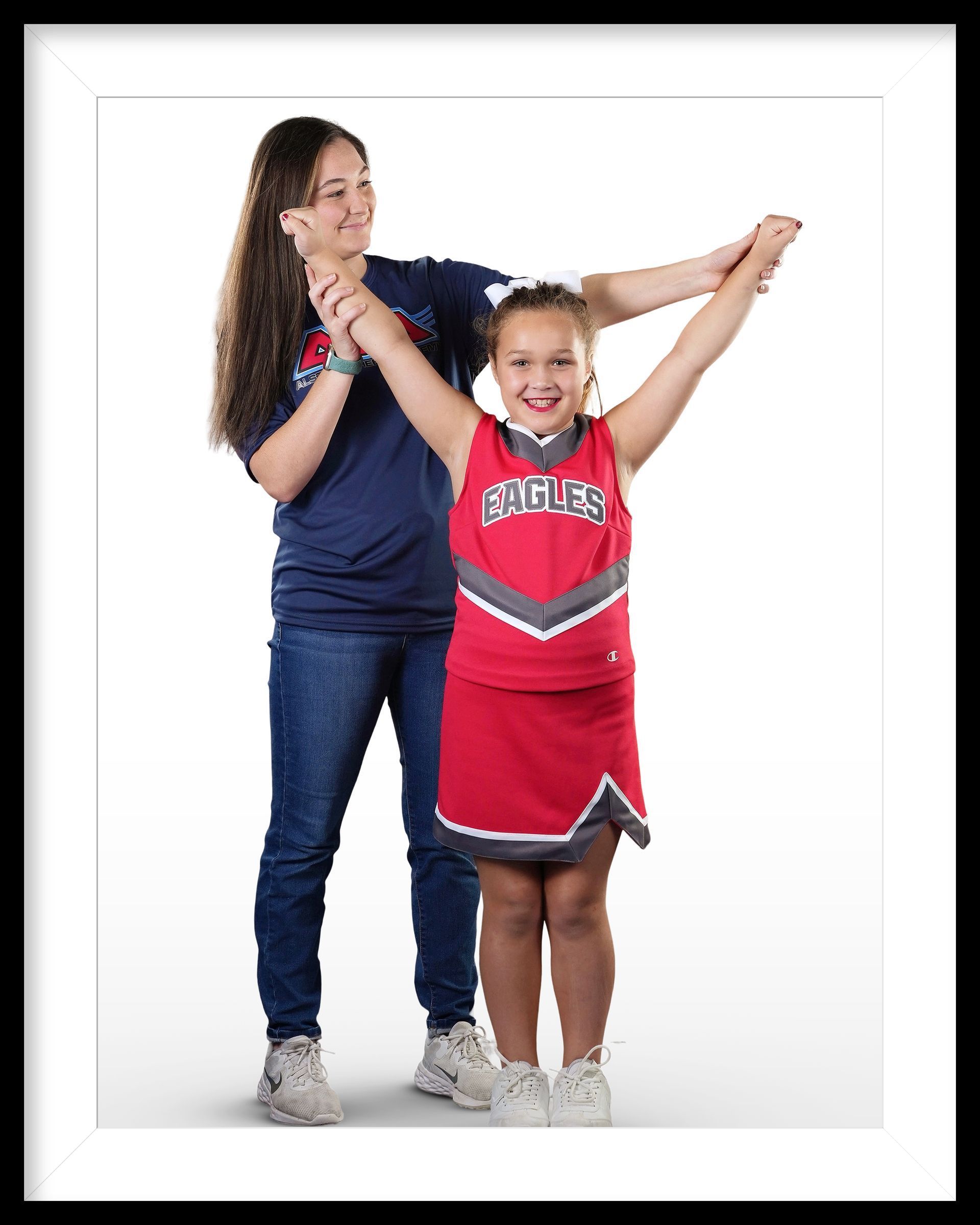 A girl in a cheerleading uniform is standing next to a girl in a blue shirt.