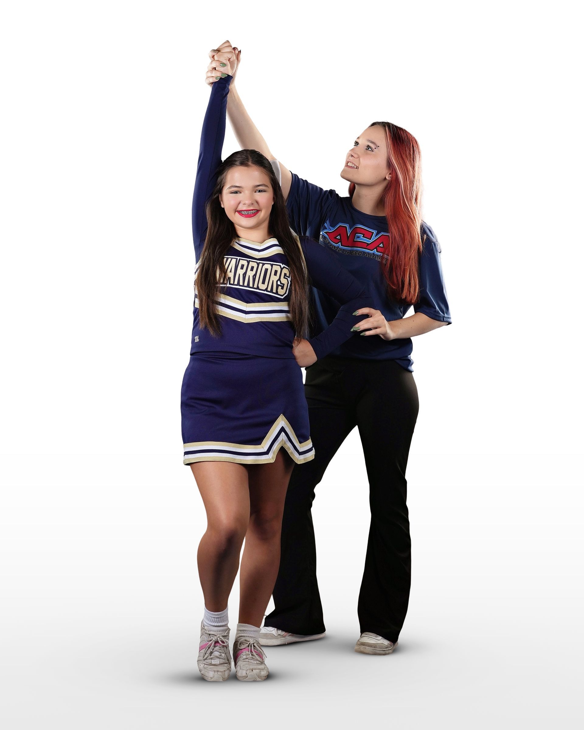 Two cheerleaders are standing next to each other with their arms in the air.