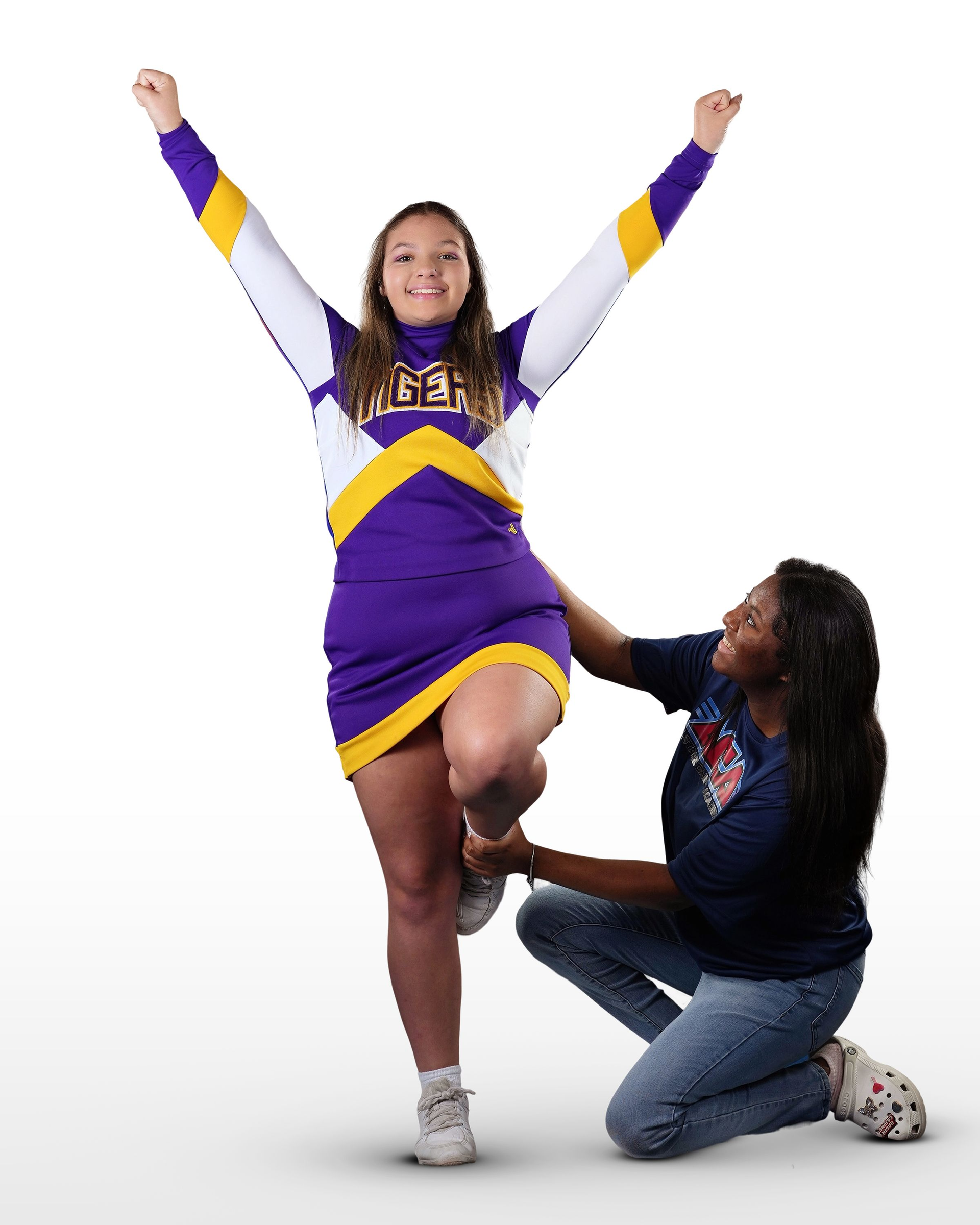 A cheerleader in a purple and yellow uniform is being helped by another cheerleader