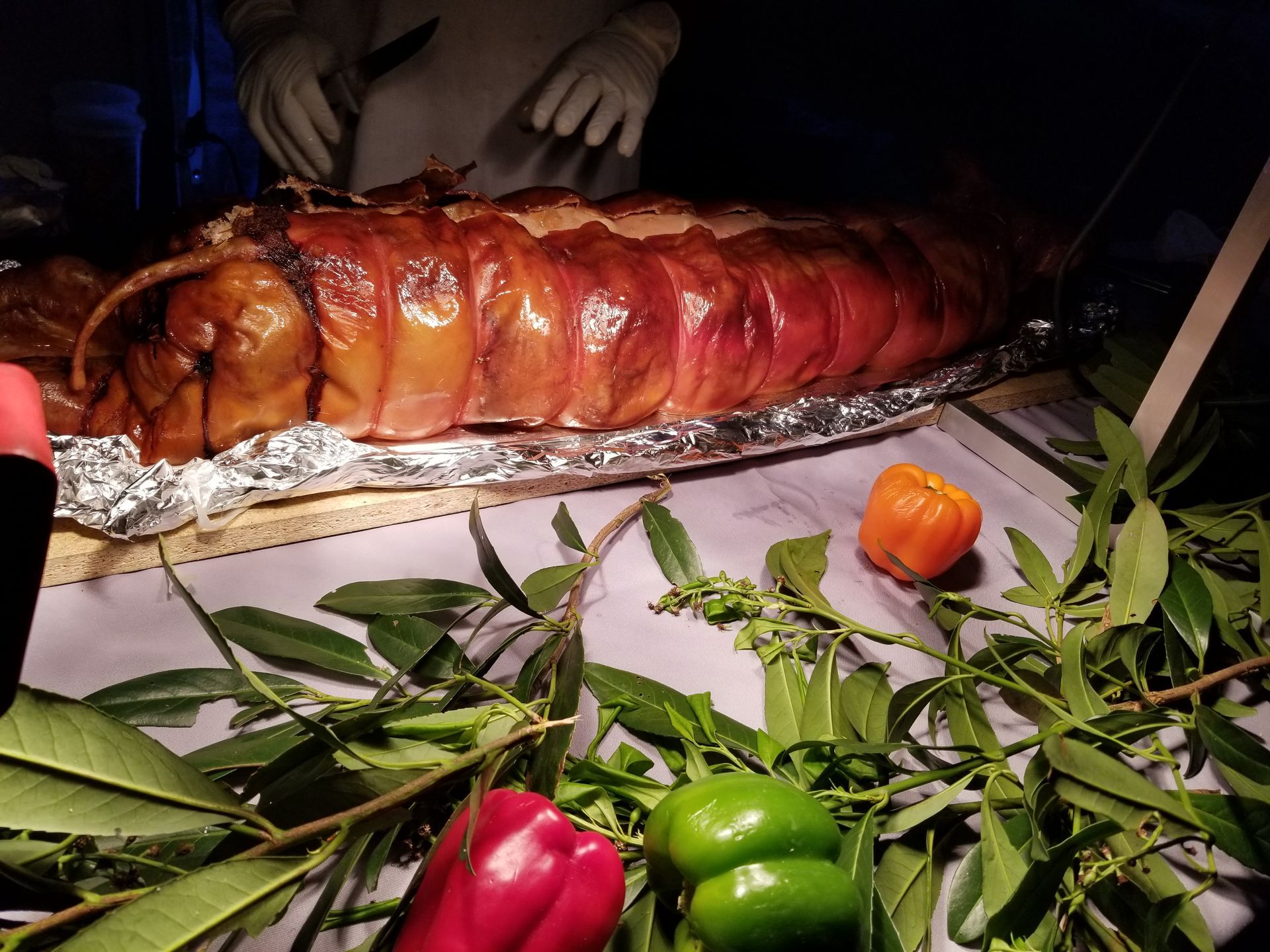 A large piece of meat is sitting on a table surrounded by peppers and leaves